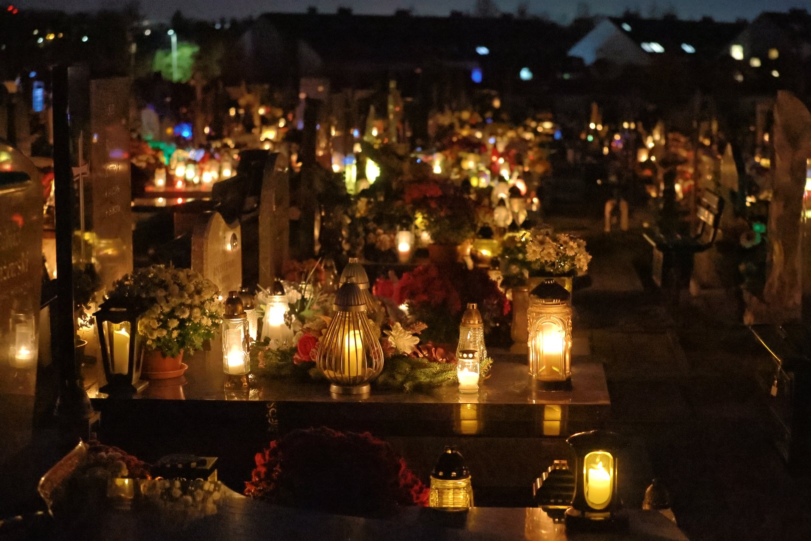 a grave lit with numerous cemetery lights with other illuminated graves in the background on All Saints' Day in Poland
