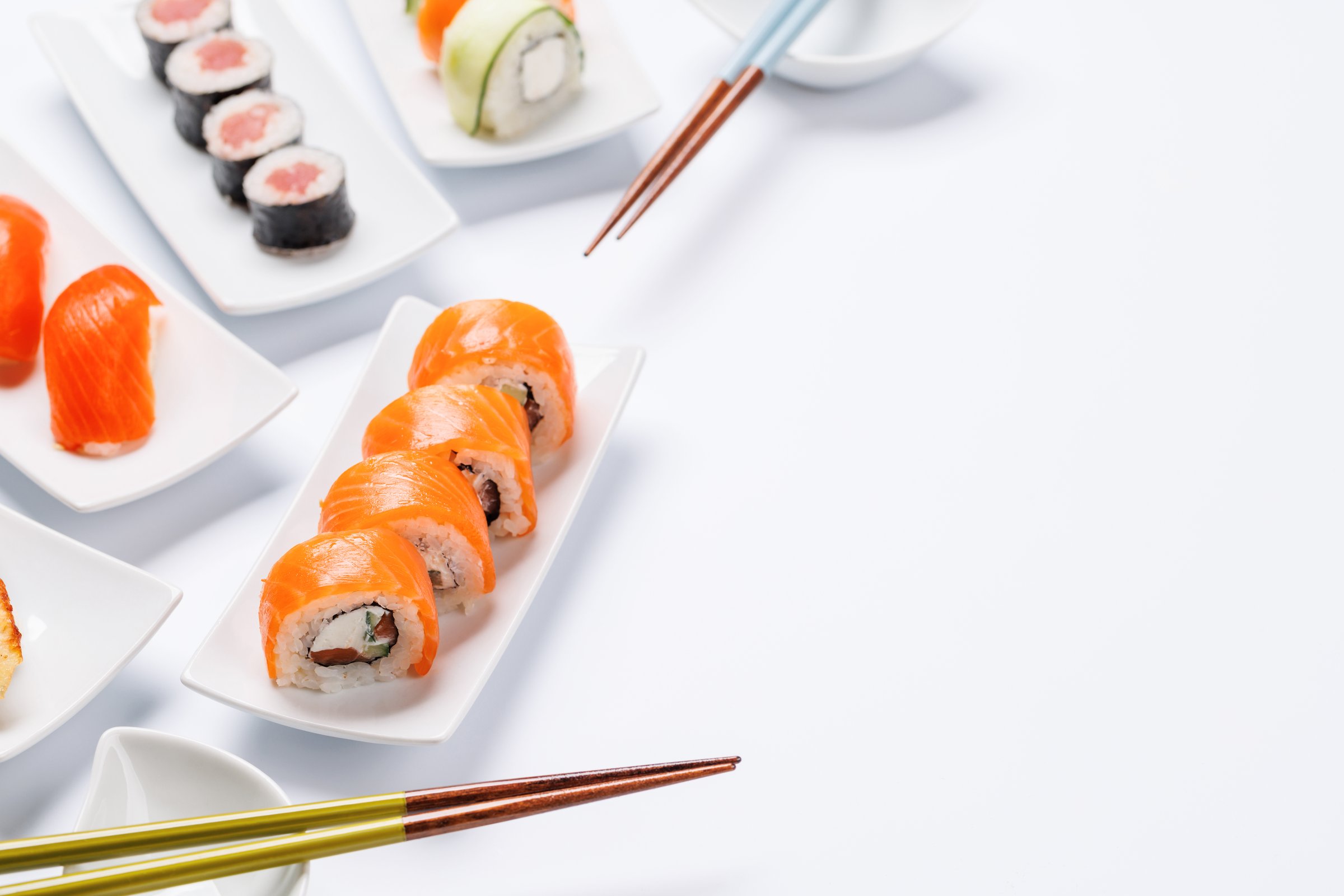 Assorted sushi and maki rolls beautifully arranged on plates, featuring fresh ingredients and vibrant colors, on a clean white background with copy space