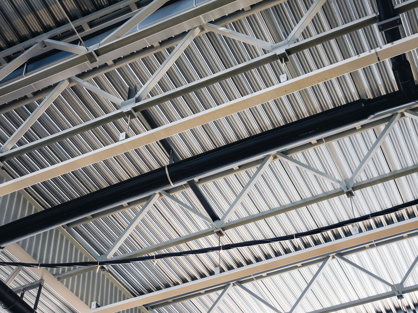 An overhead view of a metal roof with support beams and conduits. The pattern of the corrugated metal creates an interesting visual texture.