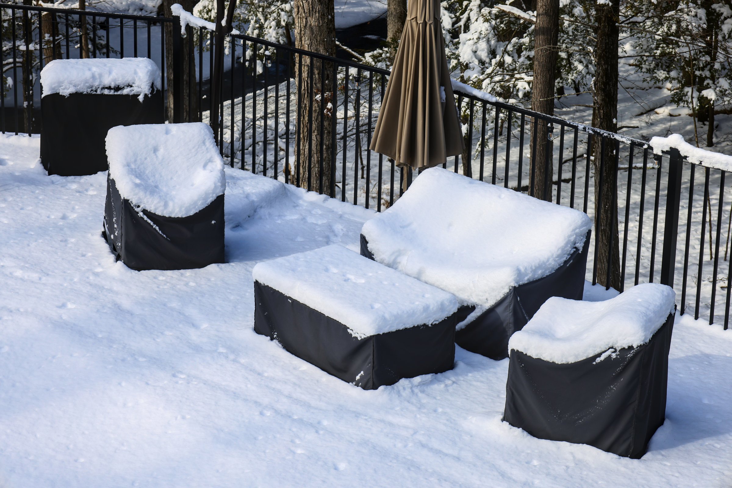 outdoor furniture in back yard covered in snow (poolside patio couch chair coffee table) chairs seating cushion cover protection from elements rain wind snowy weather (folded umbrella) fenced area