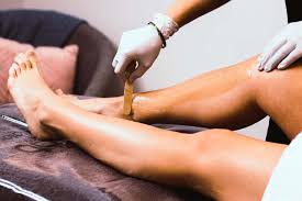 Person applying wax strip to another person's leg for hair removal in a salon setting.