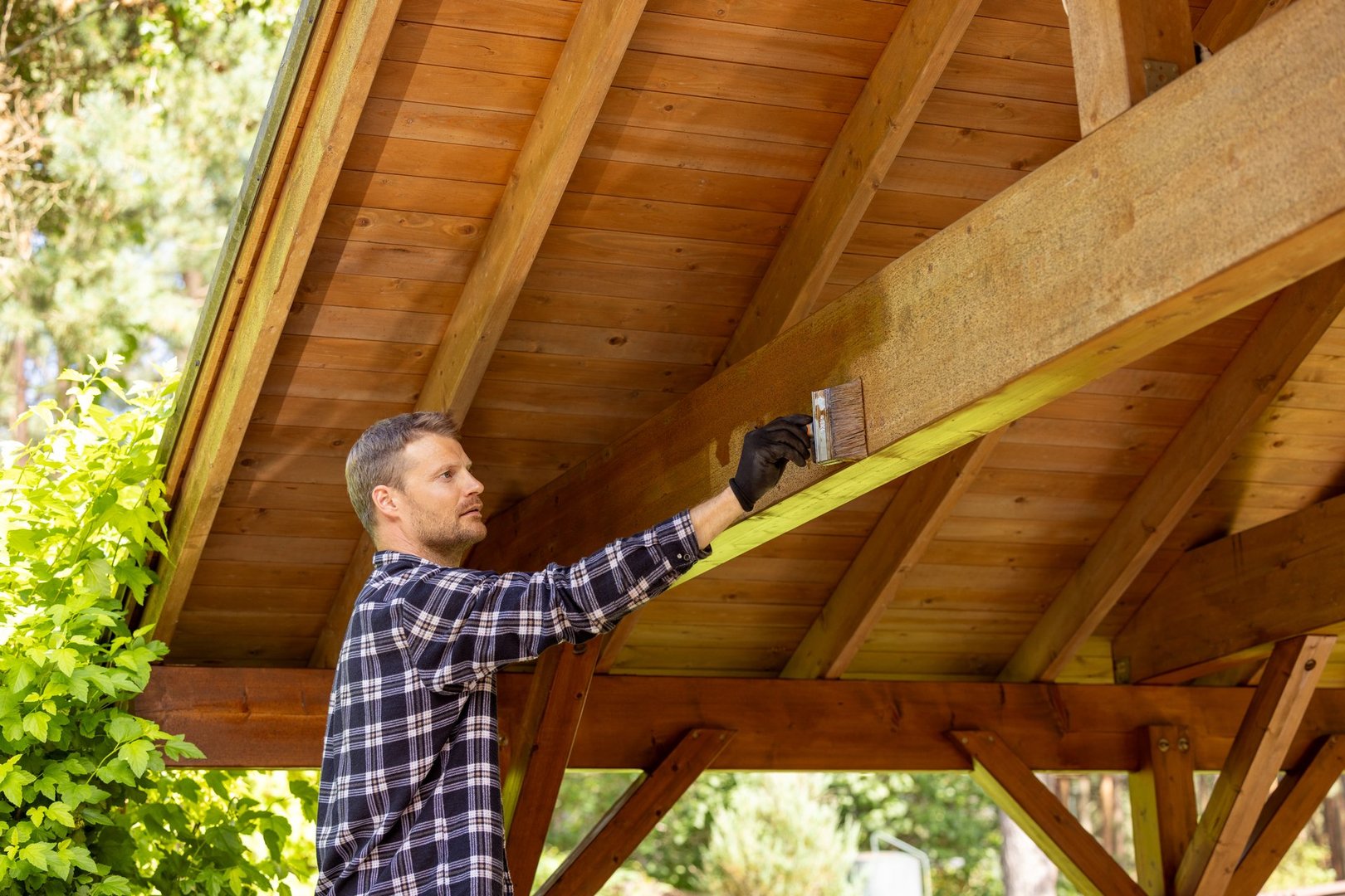 man painting timber frame outdoor carport with paintbrush and wood protective paint