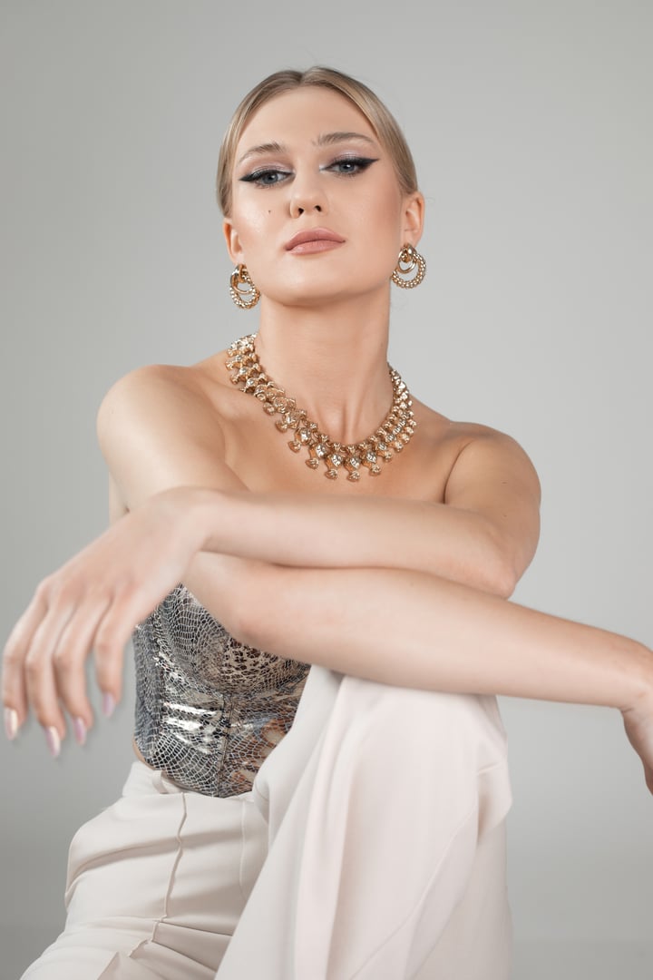 Gorgeous woman in graceful outfit with deep neckline, luxury necklace and evening makeup, white background, copy space. Exquisite female wear for holidays. Celebration, formal event, festive look.
