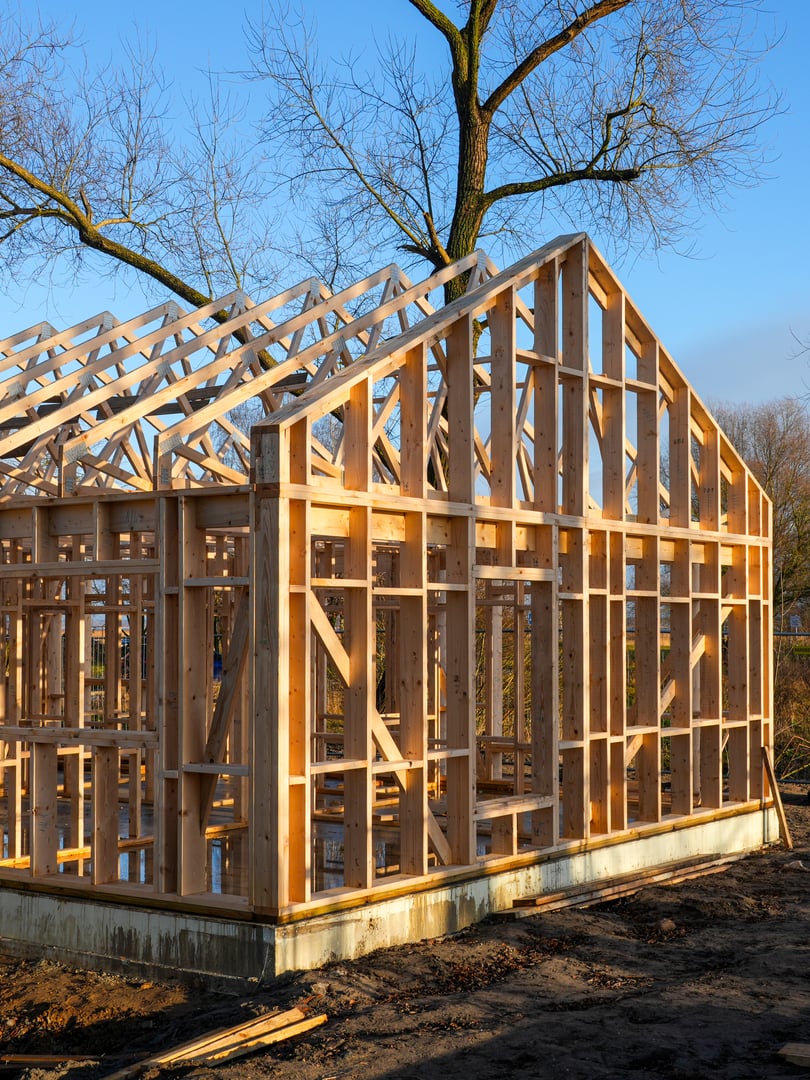 Timber frame residential house under construction on a concrete foundation, showing roof trusses and wall studs on an urban building site