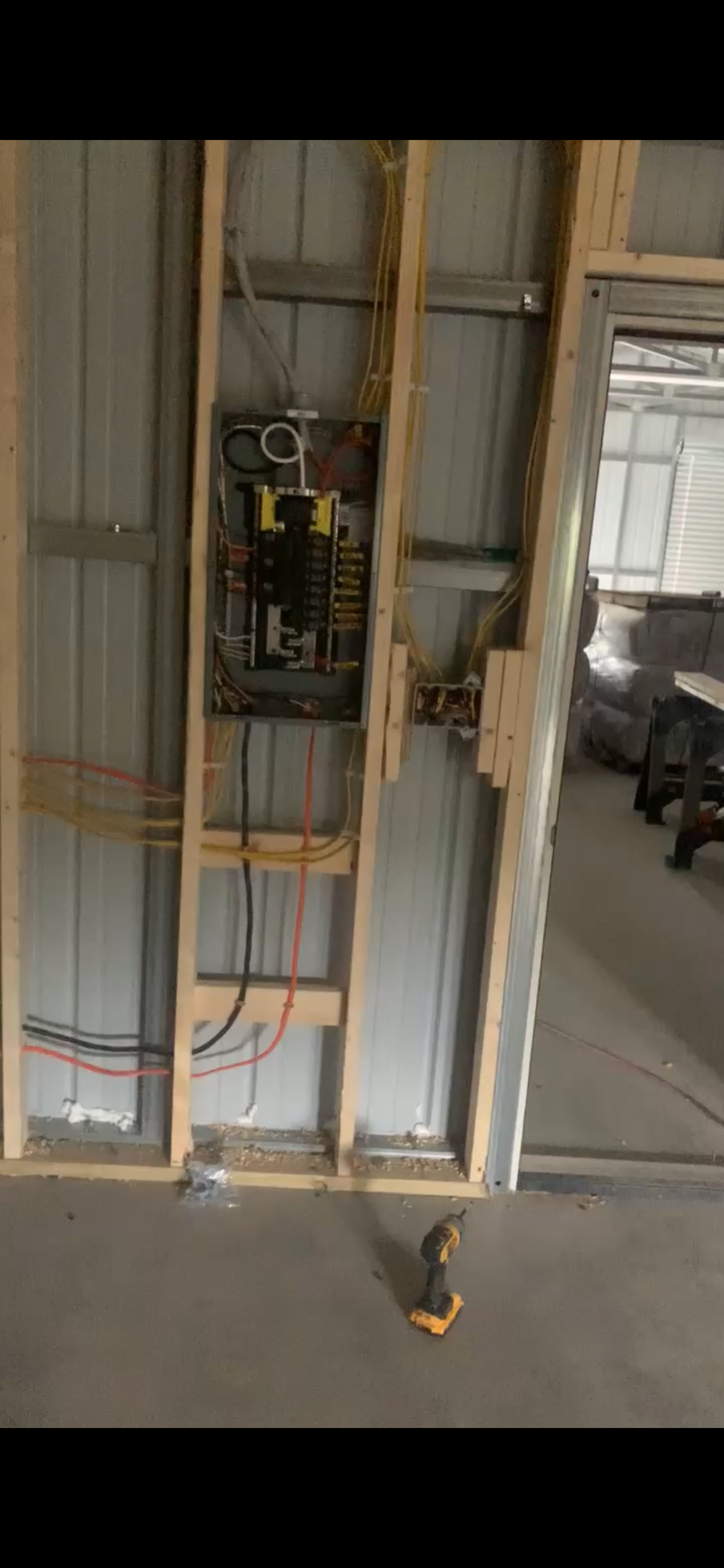 An electrical panel installation inside a partially constructed wall, with visible wiring and construction materials.