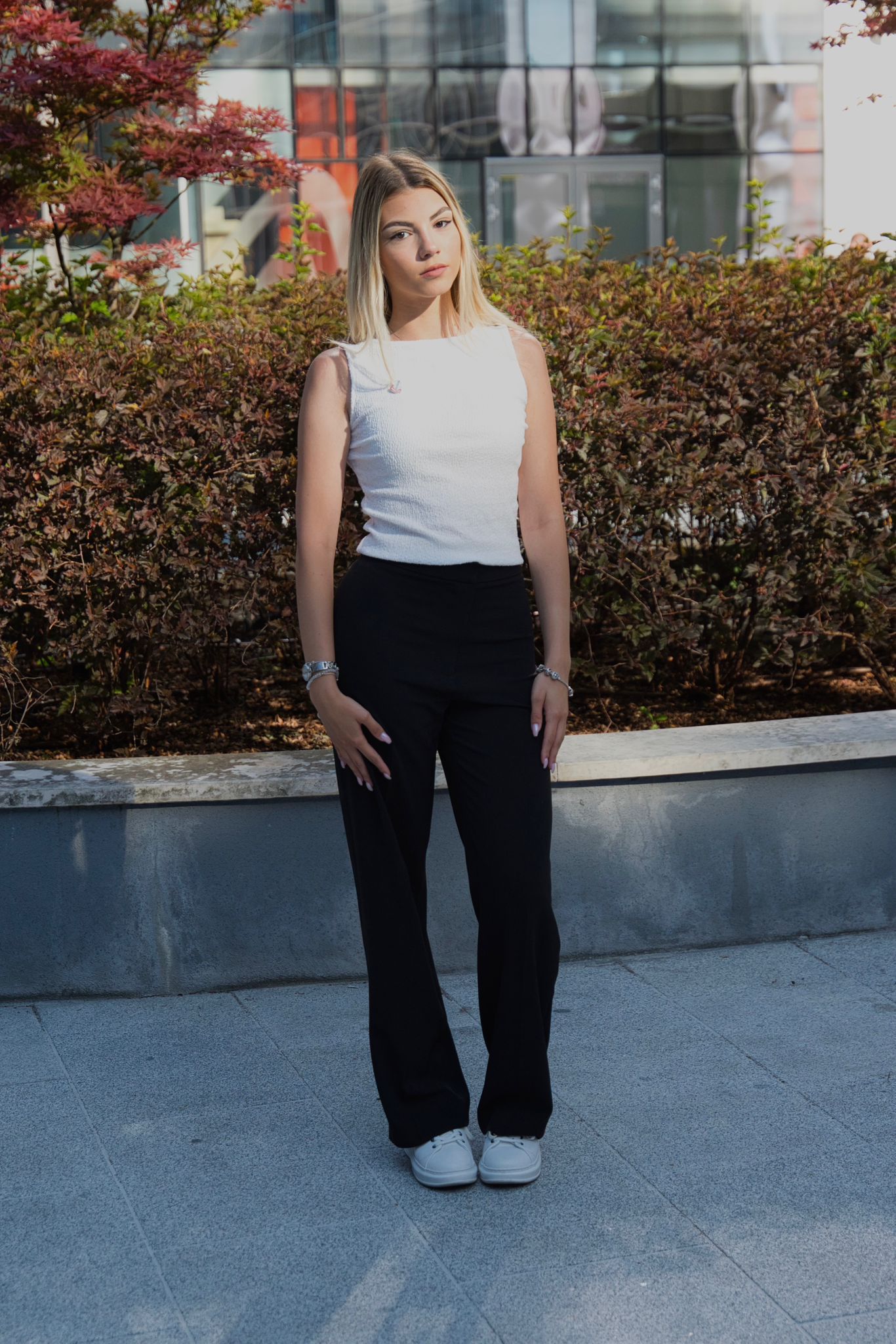 Woman with long blonde hair wearing a black top, posing with her hand on her hair.