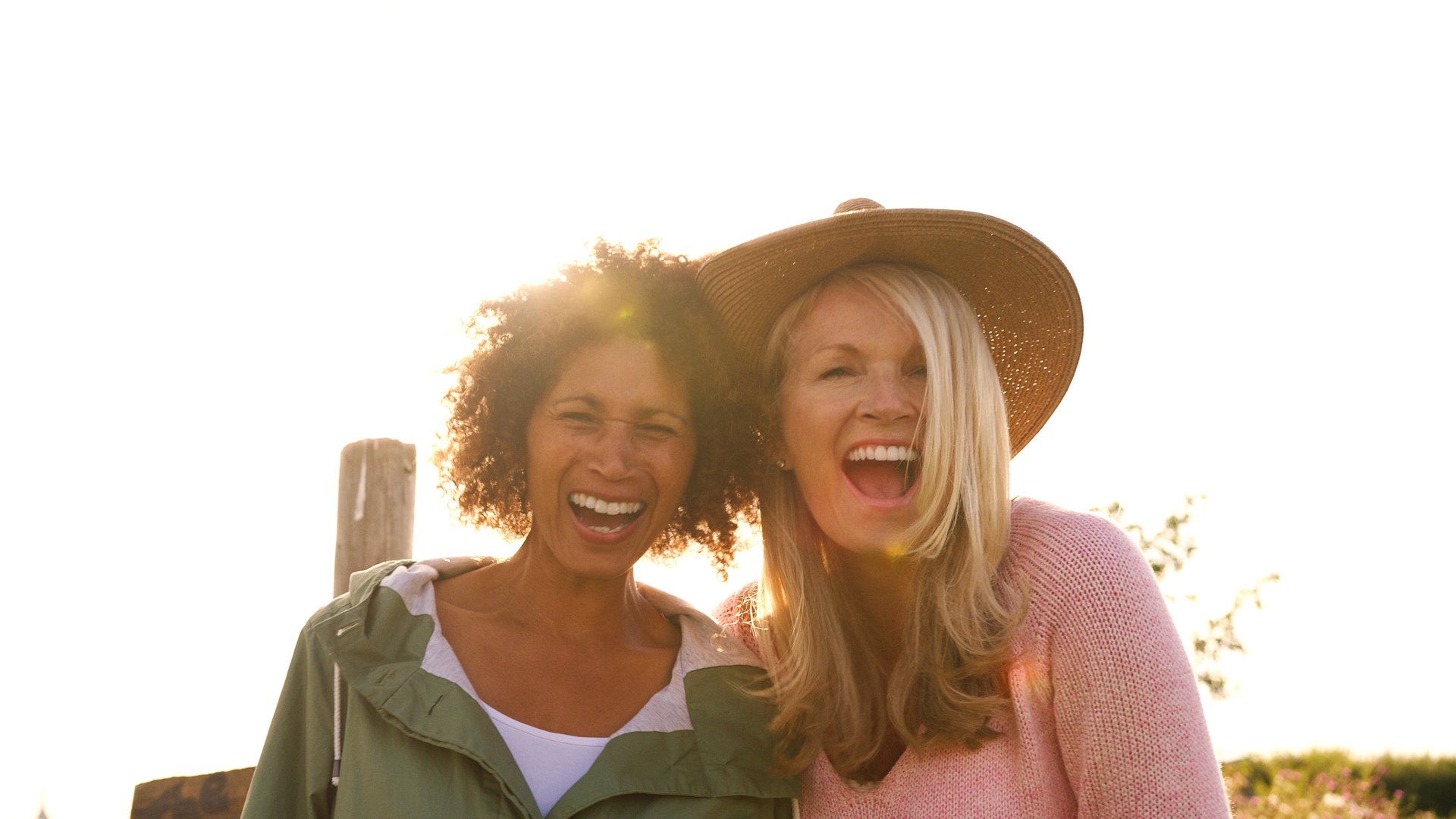 Two mature female friends smiling into camera against flaring sun