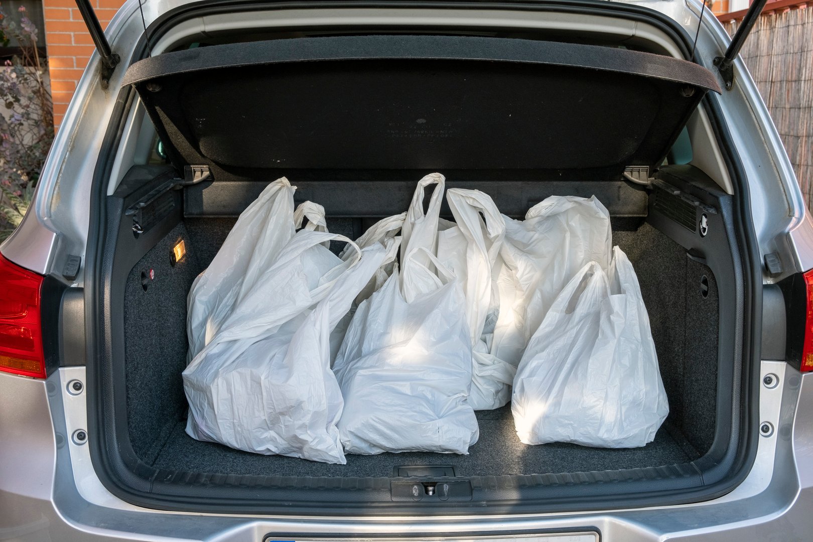 An open car trunk displaying multiple white plastic shopping bags filled with groceries and items, representing practical shopping, convenience, and transport. Ideal for illustrating errands, modern lifestyles, and household activities.