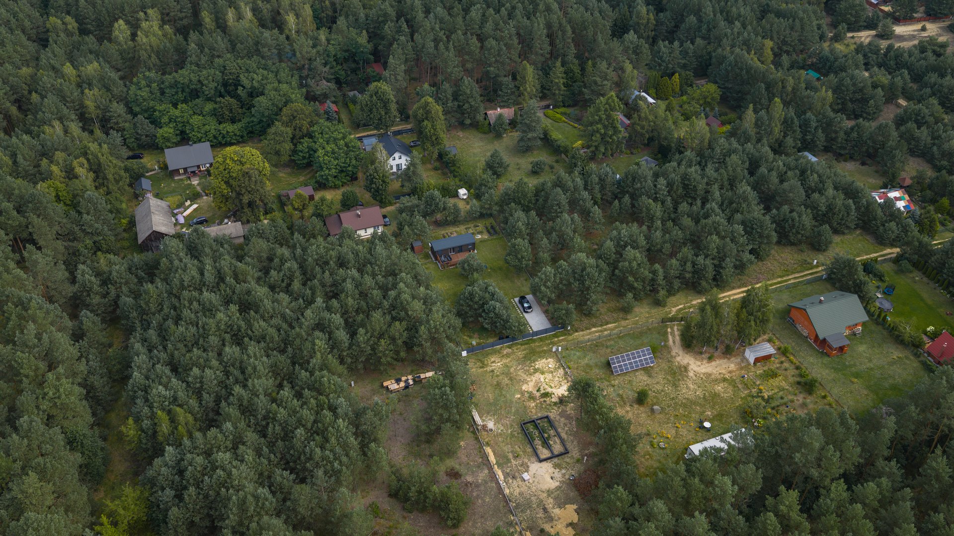 Drone view of a forest near Nowy Lubiel, Poland, showing scattered houses with red and green roofs, open clearings, and lush greenery.
