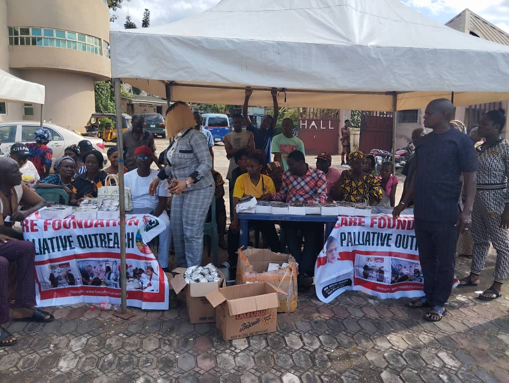 Group of people at a charity event with banners and donated items under a white tent.