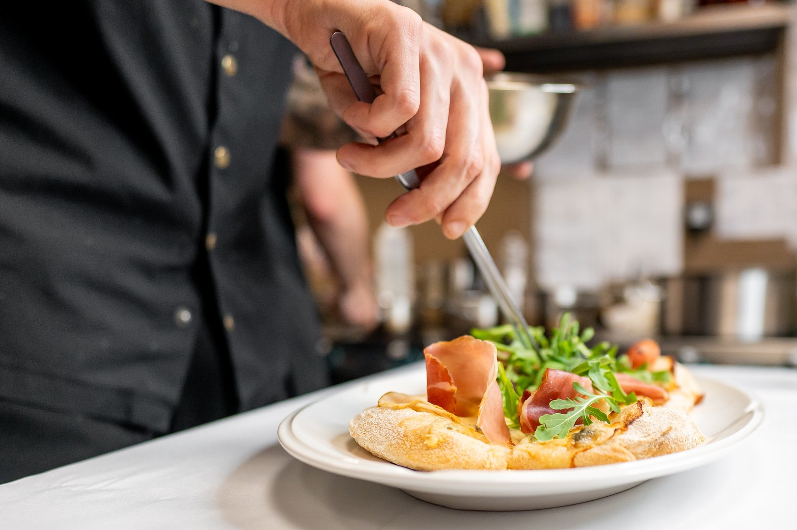 A chef skillfully prepares a gourmet dish, featuring fresh salad and savory ingredients, highlighting culinary artistry in a restaurant kitchen setting.