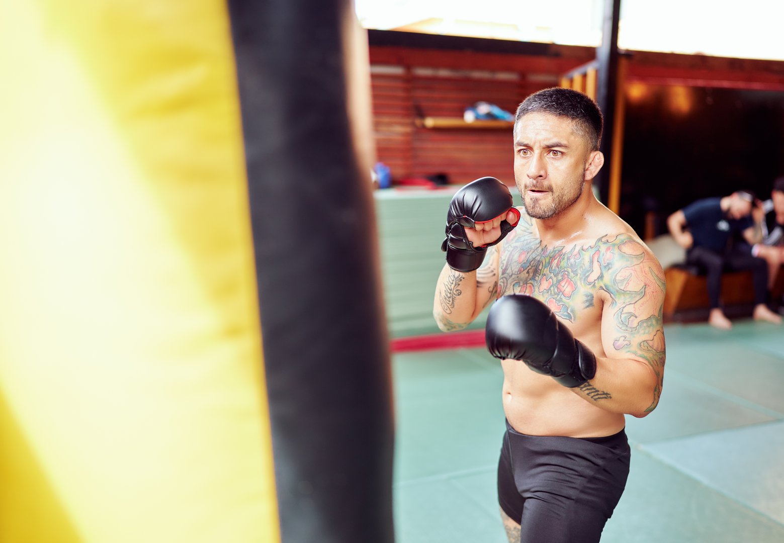 Male athlete exercising boxing punches, training with a punching bag inside a gym