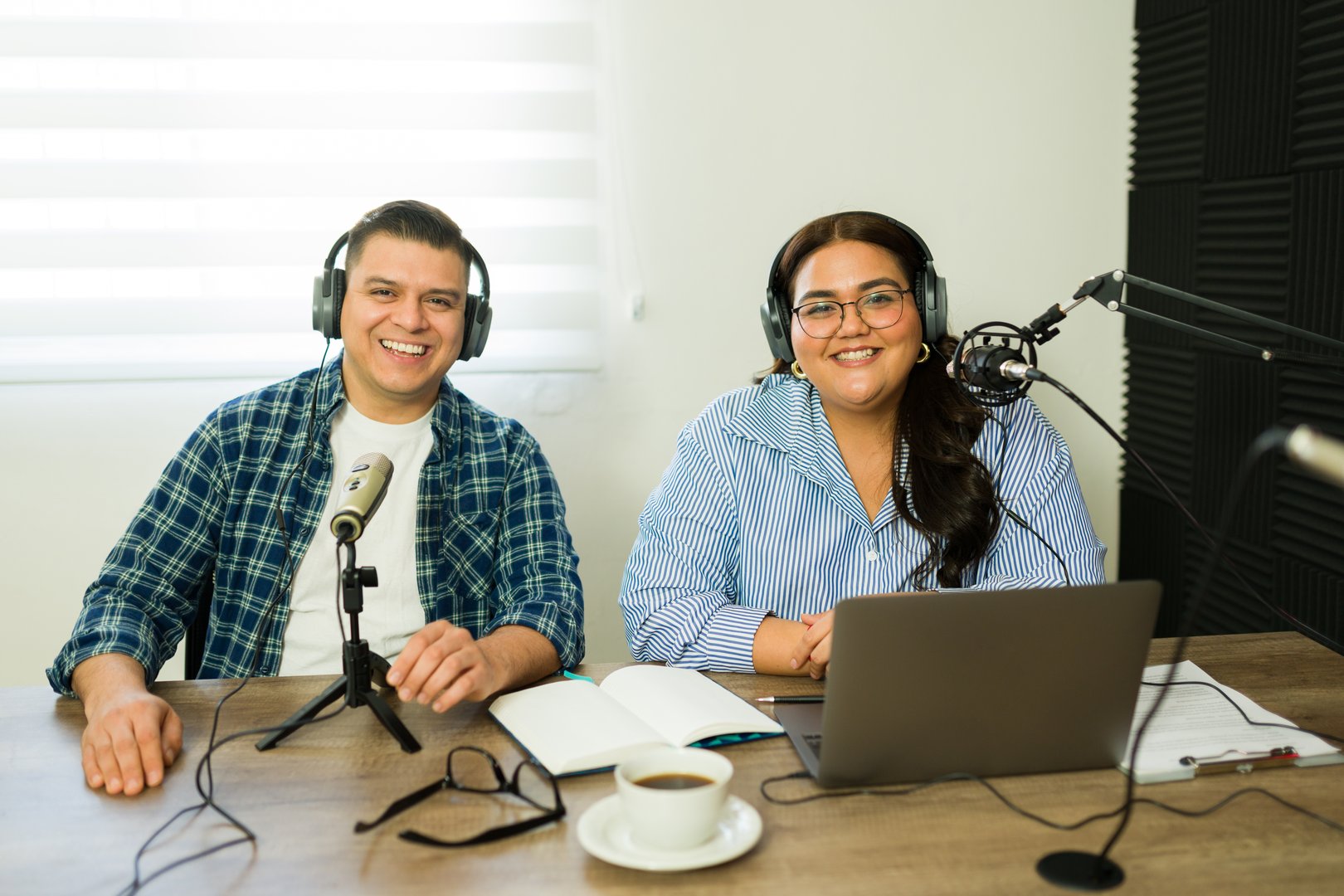 Attractive woman and man smiling while making a podcast and talking during a radio show on the microphone wearing headphones