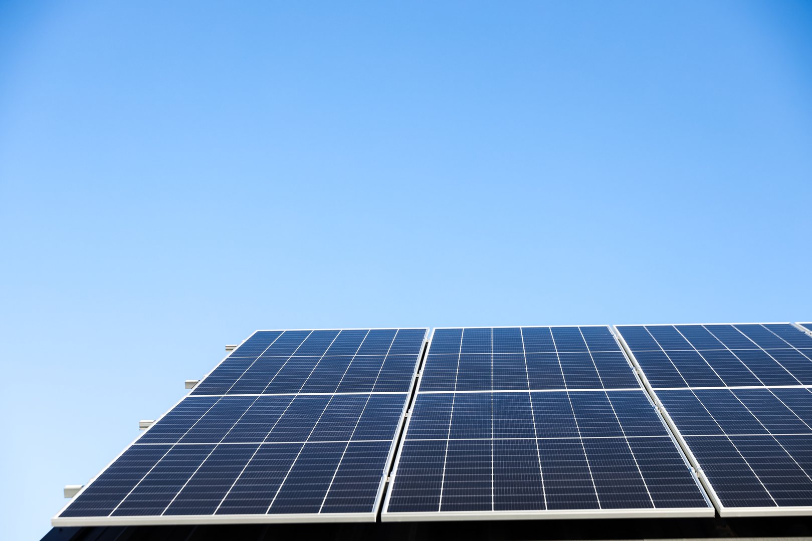 Aerial view of solar panel cells on clear blue sky background. Clean alternative energy power concept, sustainable resources. Modern house, solar panels stand-alone photovoltaic plant system on roof