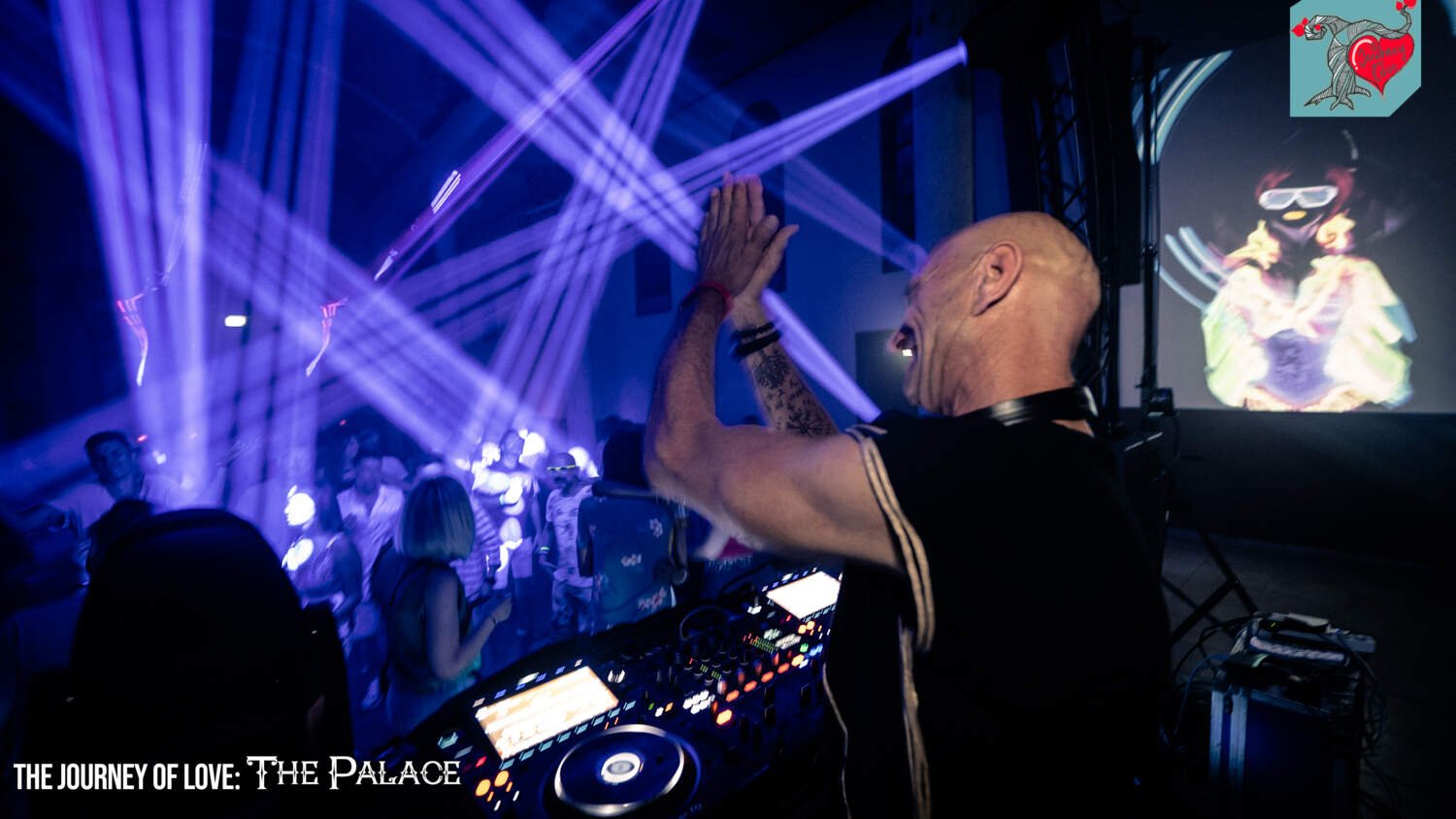DJ performing at a nightclub with laser lights and a screen displaying visuals; audience dancing in the background.
