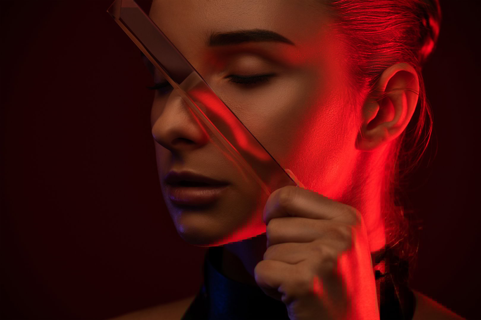 Portrait of an attractive girl with healthy clean skin and beautiful makeup in a neon light. She holds a long transparent stone near her face.