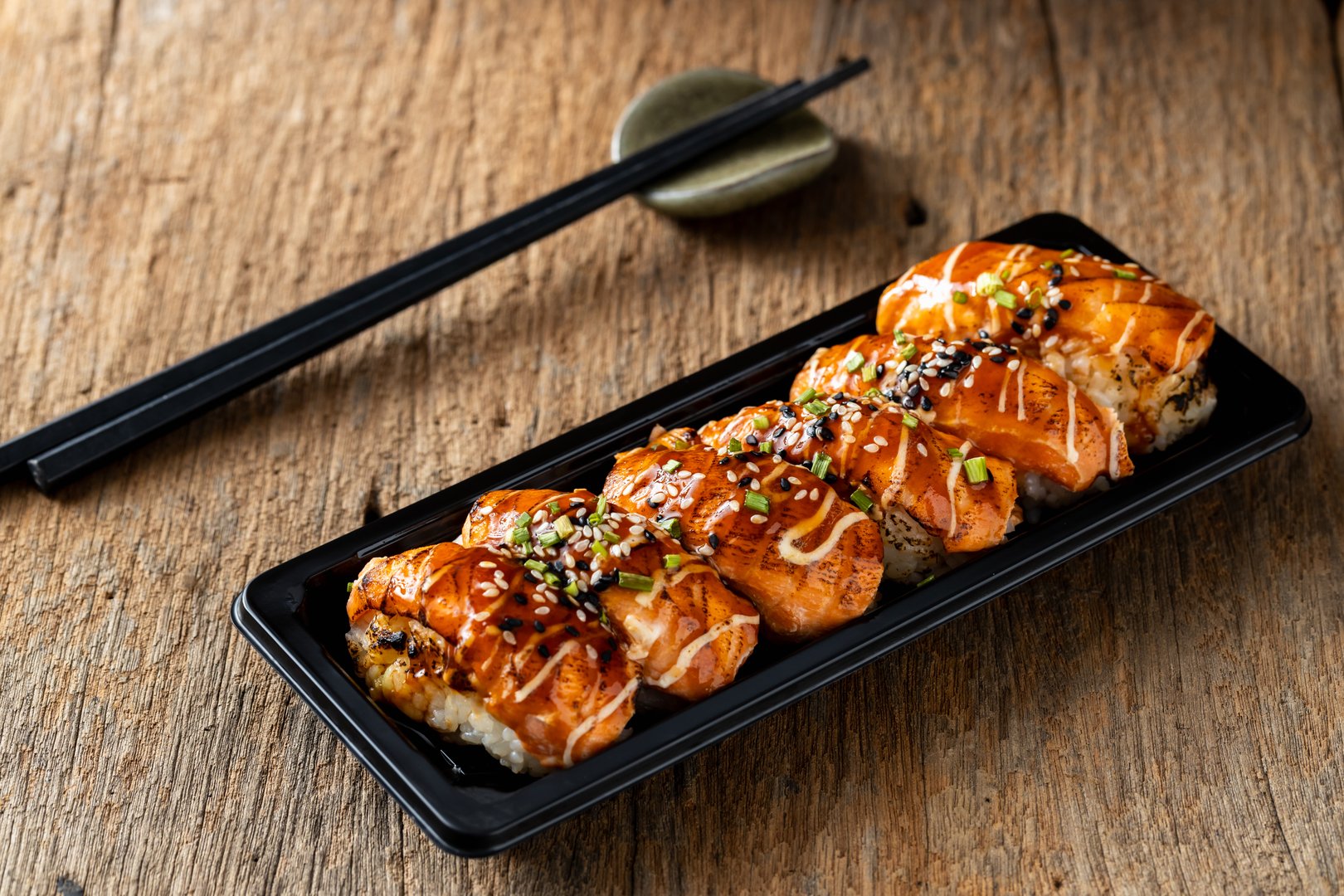 Savor a beautifully presented sushi plate featuring grilled salmon drizzled with sauce on a rustic wooden table. Perfect for culinary enthusiasts or sushi lovers.