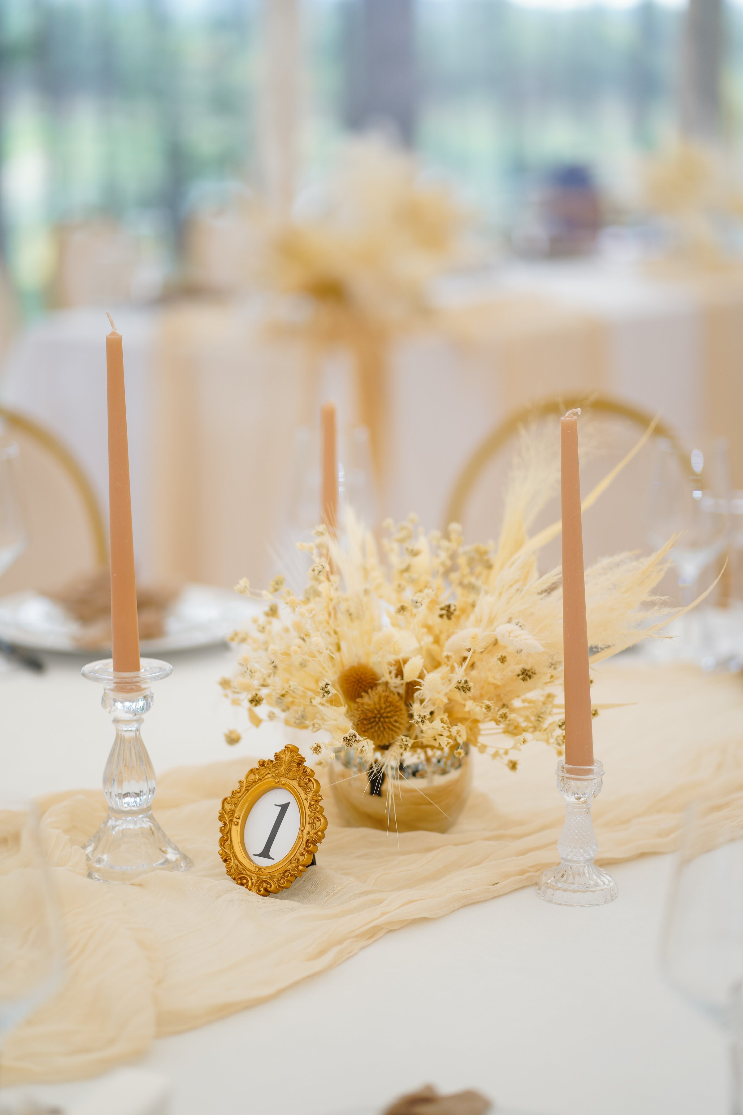 Wedding table decorated with dried flowers, candles and golden frame with number one.