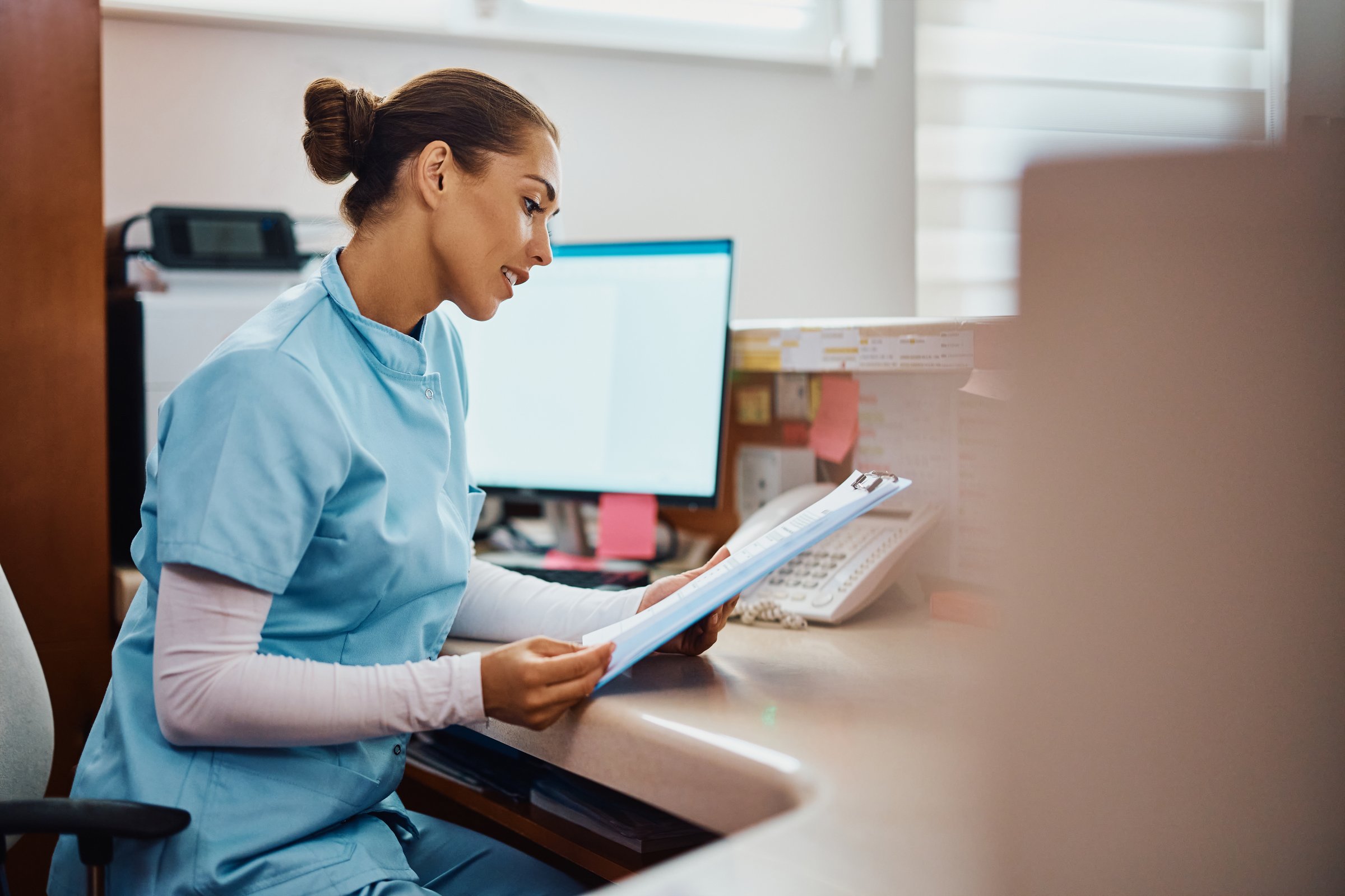 Young nurse reading medical reports while working at reception desk at doctor's office.