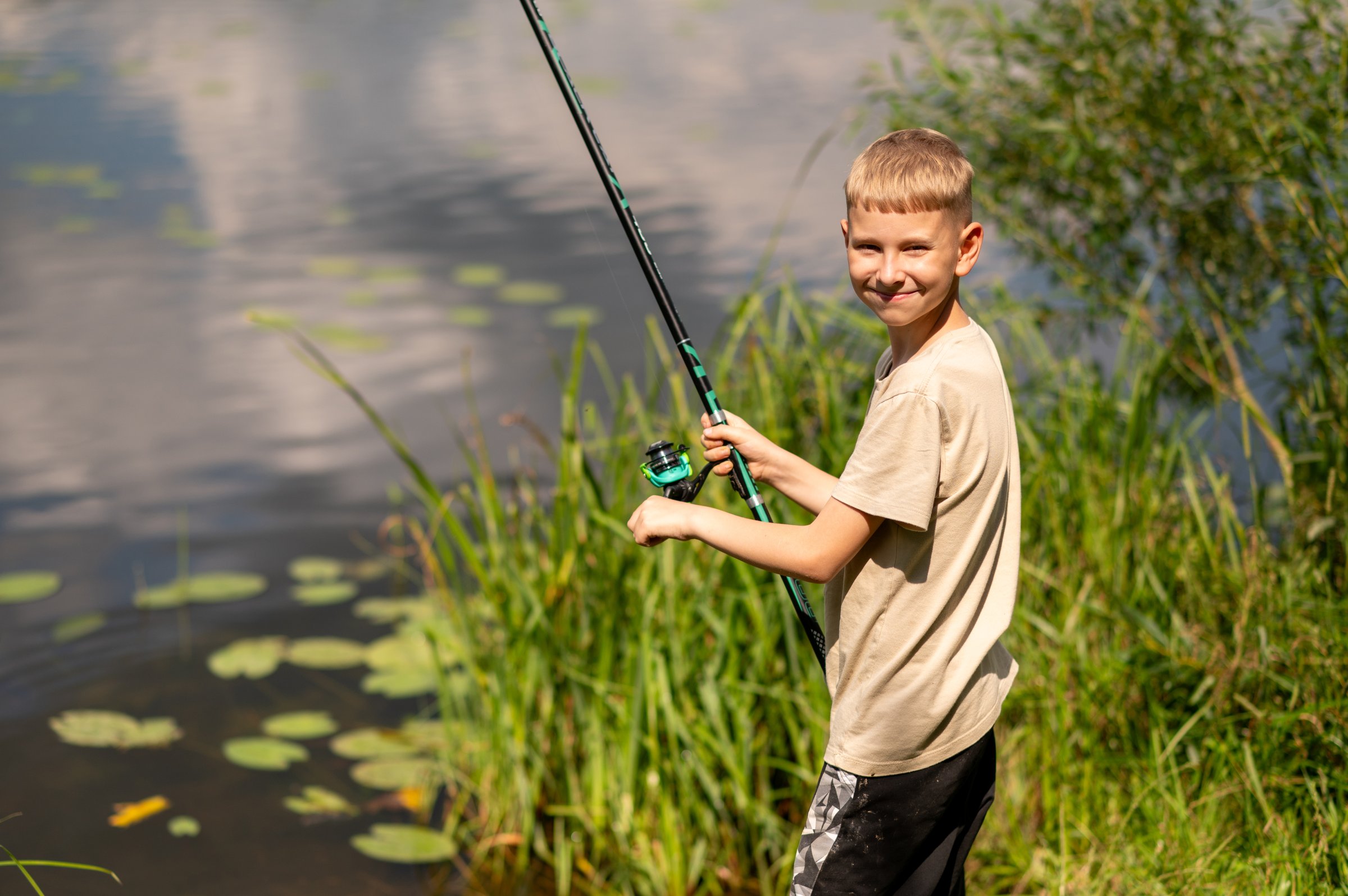 Joyful blond boy smiling while fishing on a sunny summer day