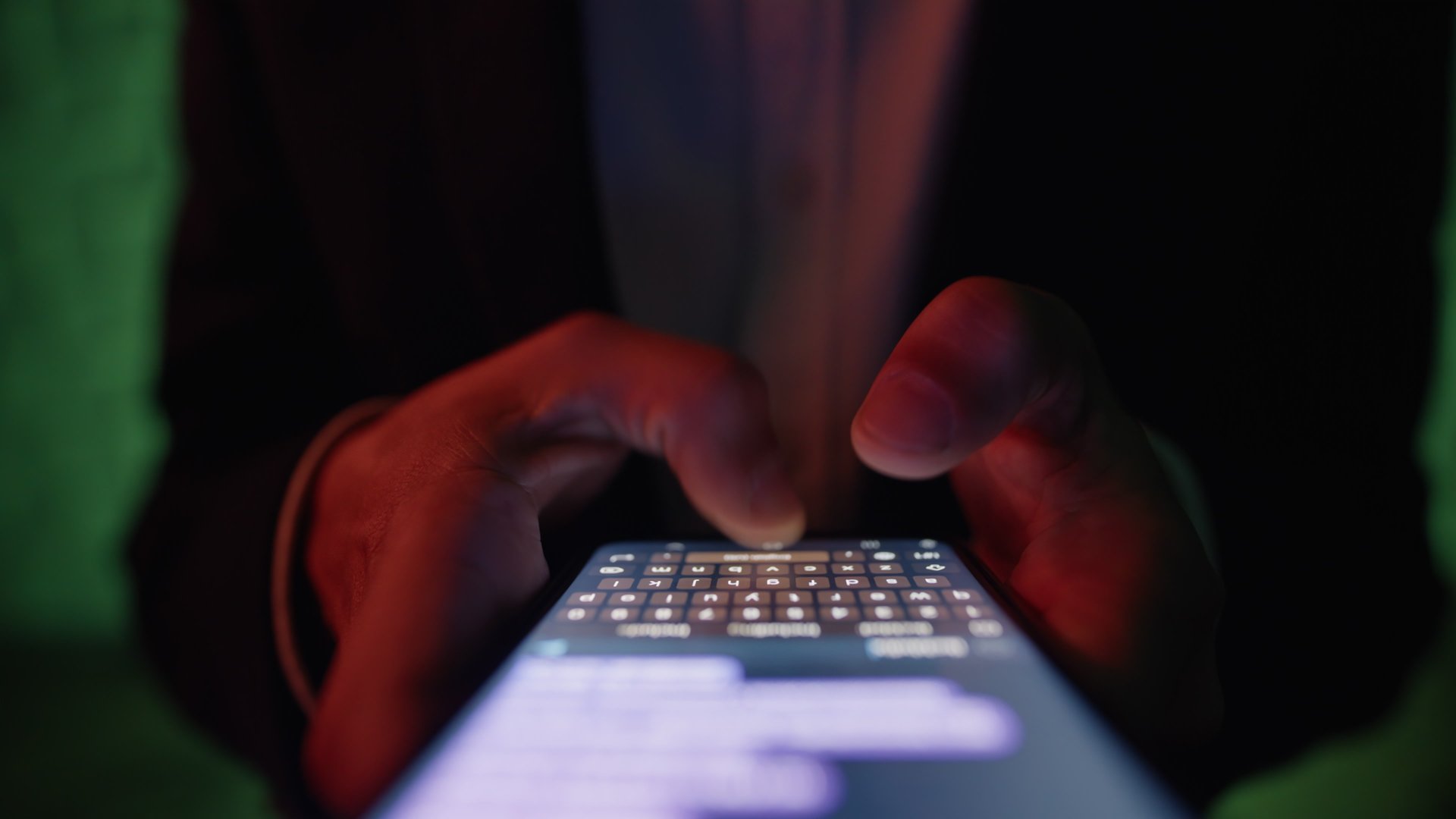 Closeup view of male fingers texting on smartphone screen. Unknown man composing message on digital keypad using chat app for communication in disco club neon light. Person holding handheld device