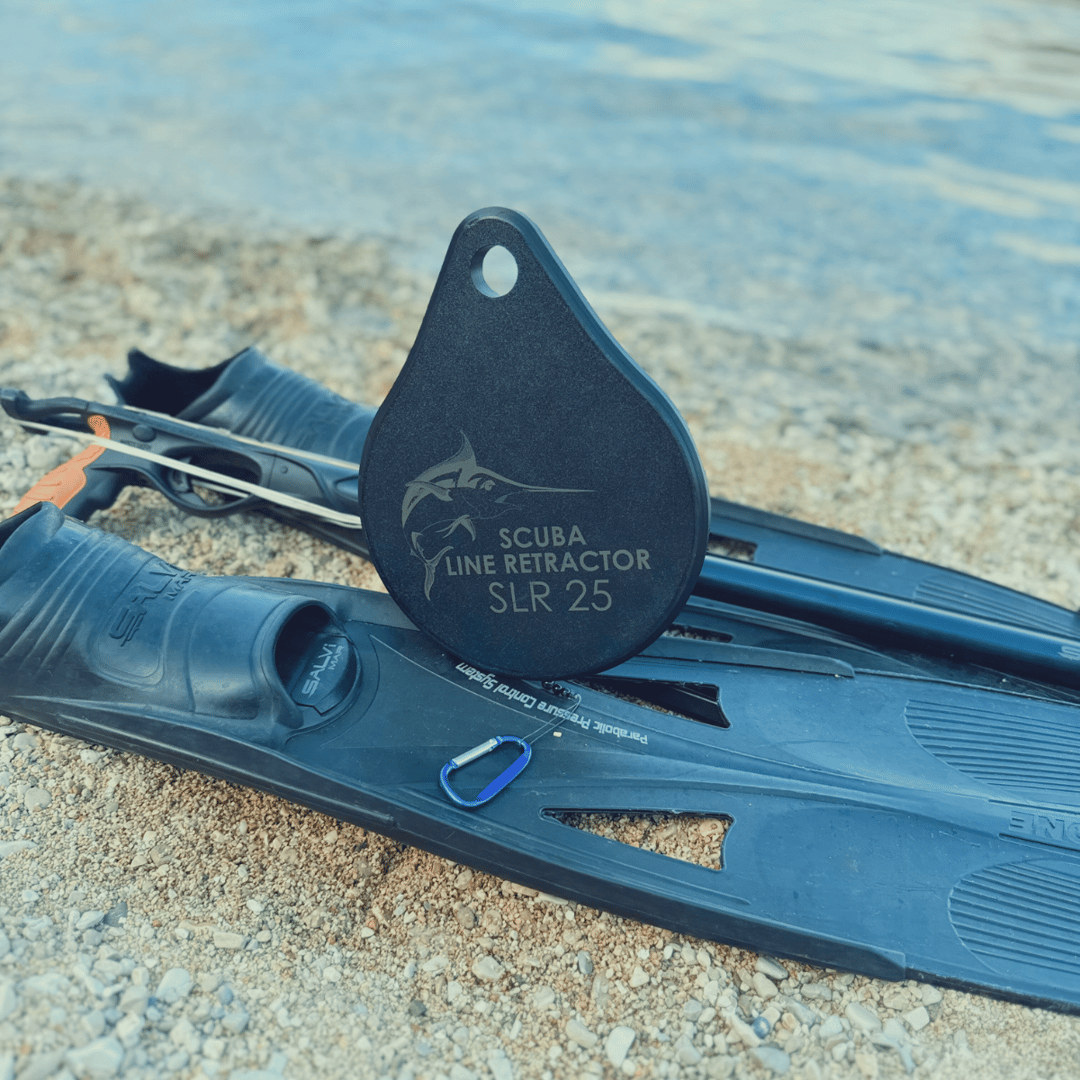 Diving fins and a scuba line retractor placed on a sandy beach near the waters edge.