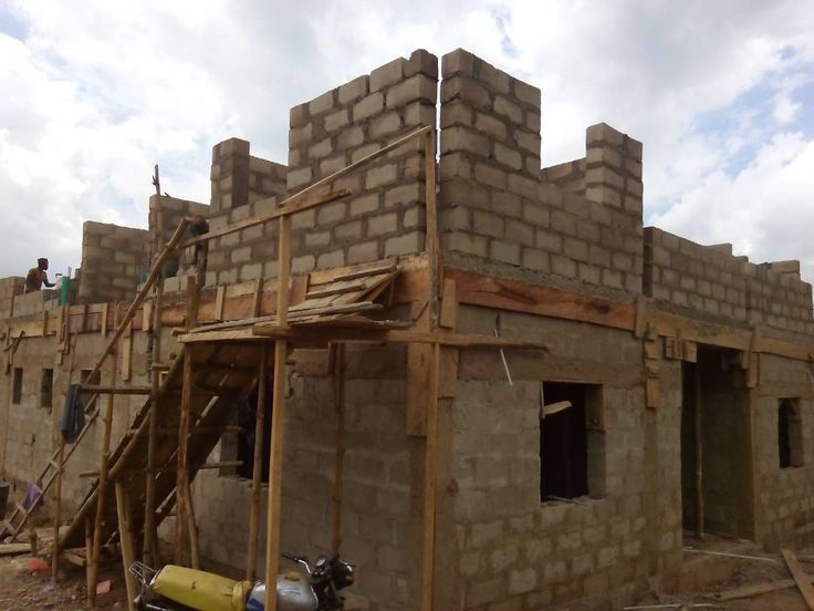 Partially constructed brick building with scaffolding and two visible windows under a cloudy sky.
