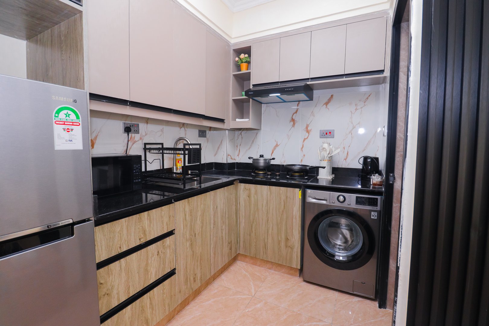 Modern kitchen with wood cabinets, black countertops, stainless steel fridge, washing machine, and marble backsplash.