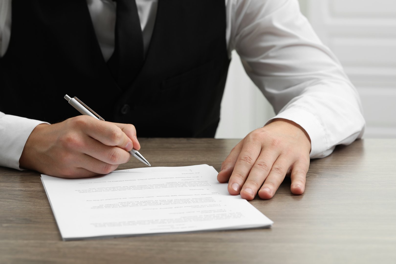 Man signing document at wooden table, closeup