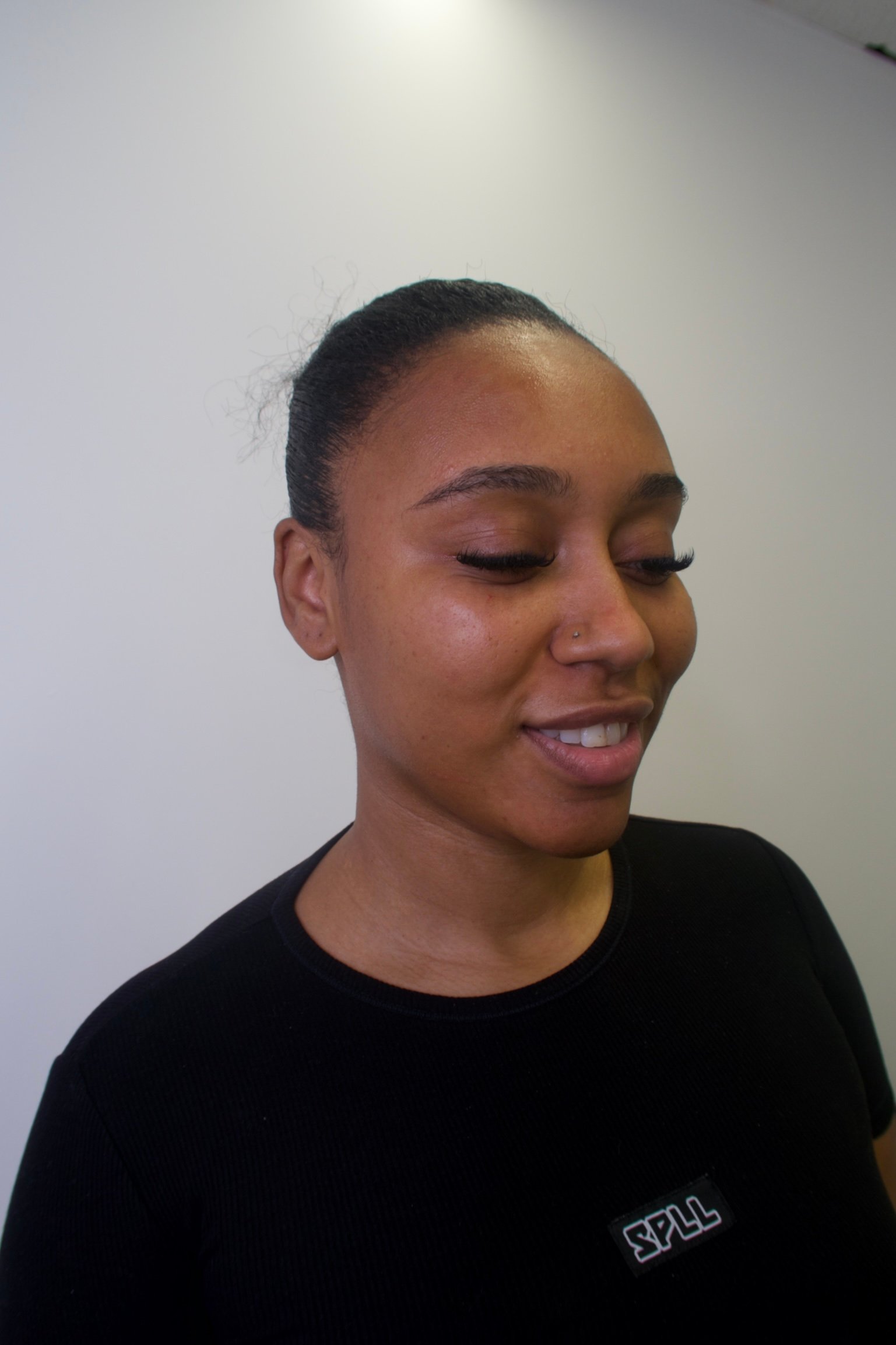 A woman with braided hair, wearing a black shirt, stands against a plain white background, smiling slightly to the side.