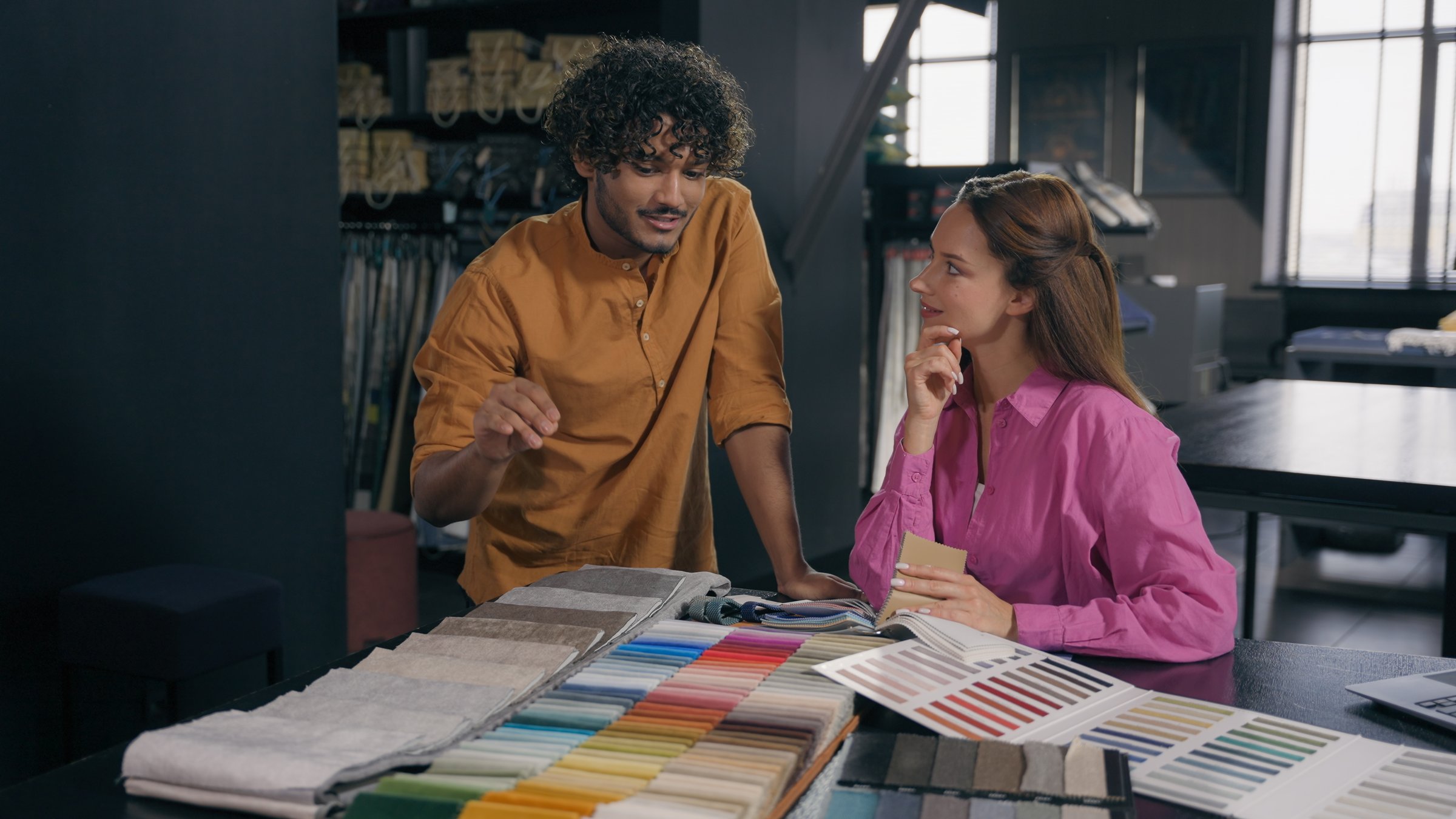 Multiracial couple buyers choosing fabric samples collection buying cloth in atelier Arabian Indian man salesman fashion designer consult Caucasian woman customer discuss choose materials house design. High quality 4k footage
