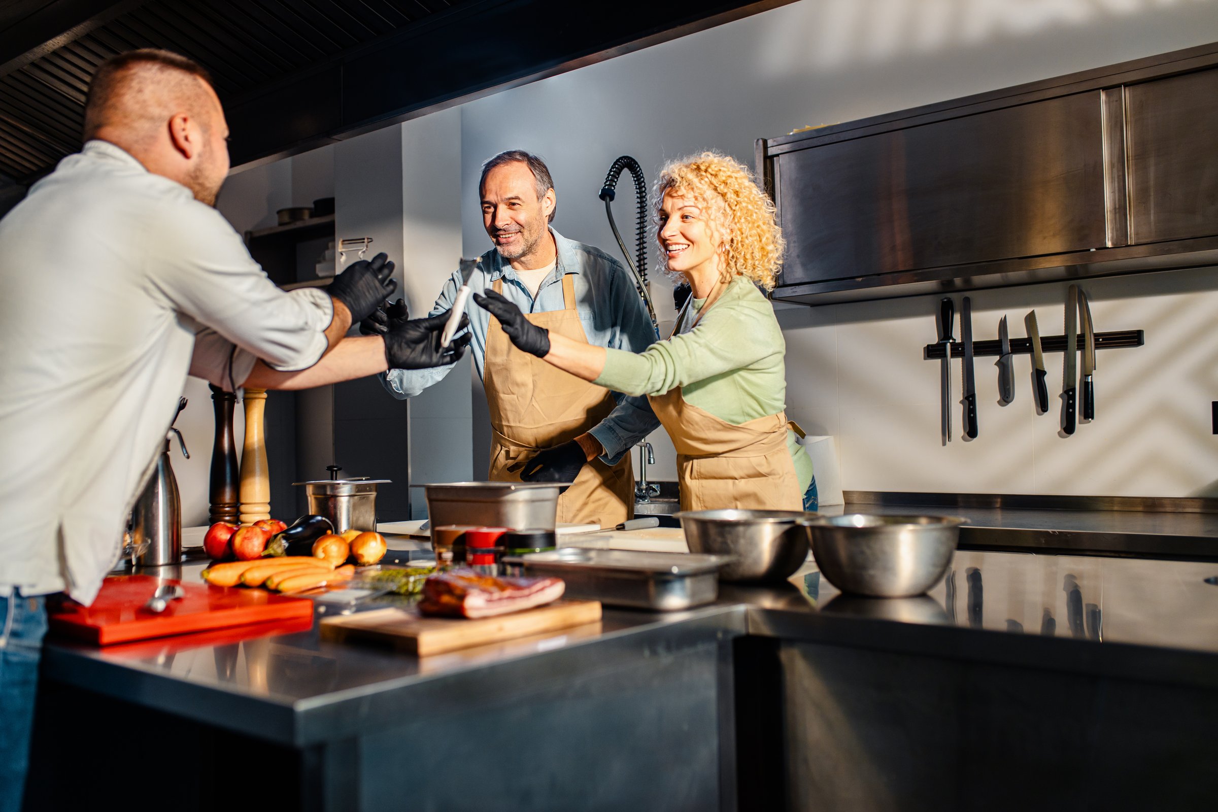 Middle-aged couple enjoying a cooking class with a chef preparing carrot for a meal in the kitchen.