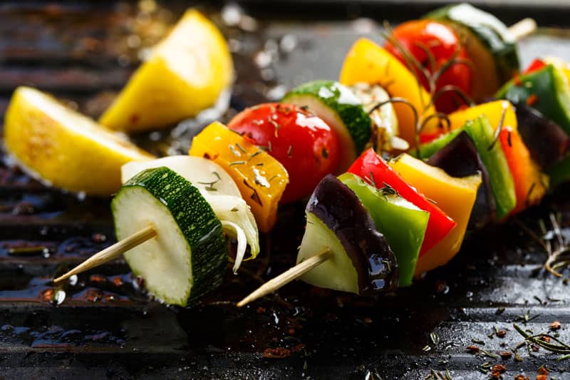 Grilled vegetable skewers with zucchini, bell peppers, and cherry tomatoes, garnished with rosemary, on a grill pan.