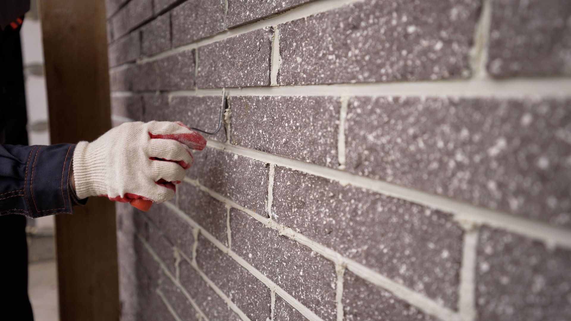 The worker wipes the brickwork of the wall, the bricklayer wipes the seam between the bricks. The builder carefully makes a brick wall, a close-up of a skilled craftsman laying a large masonry of bricks, the concept of a building, builds a house.
