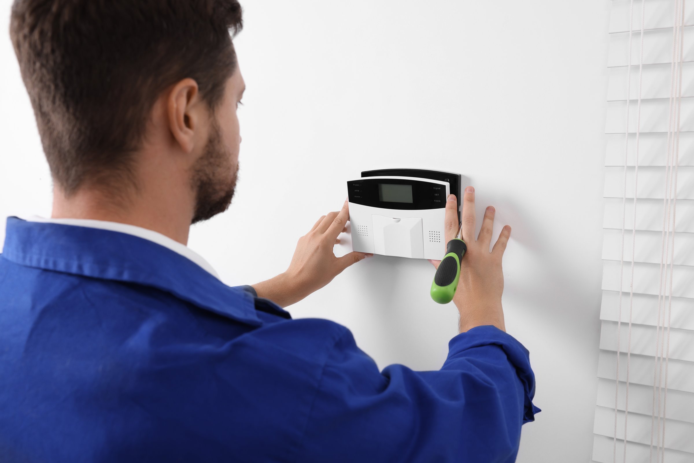 Technician installing home security alarm system on white wall indoors