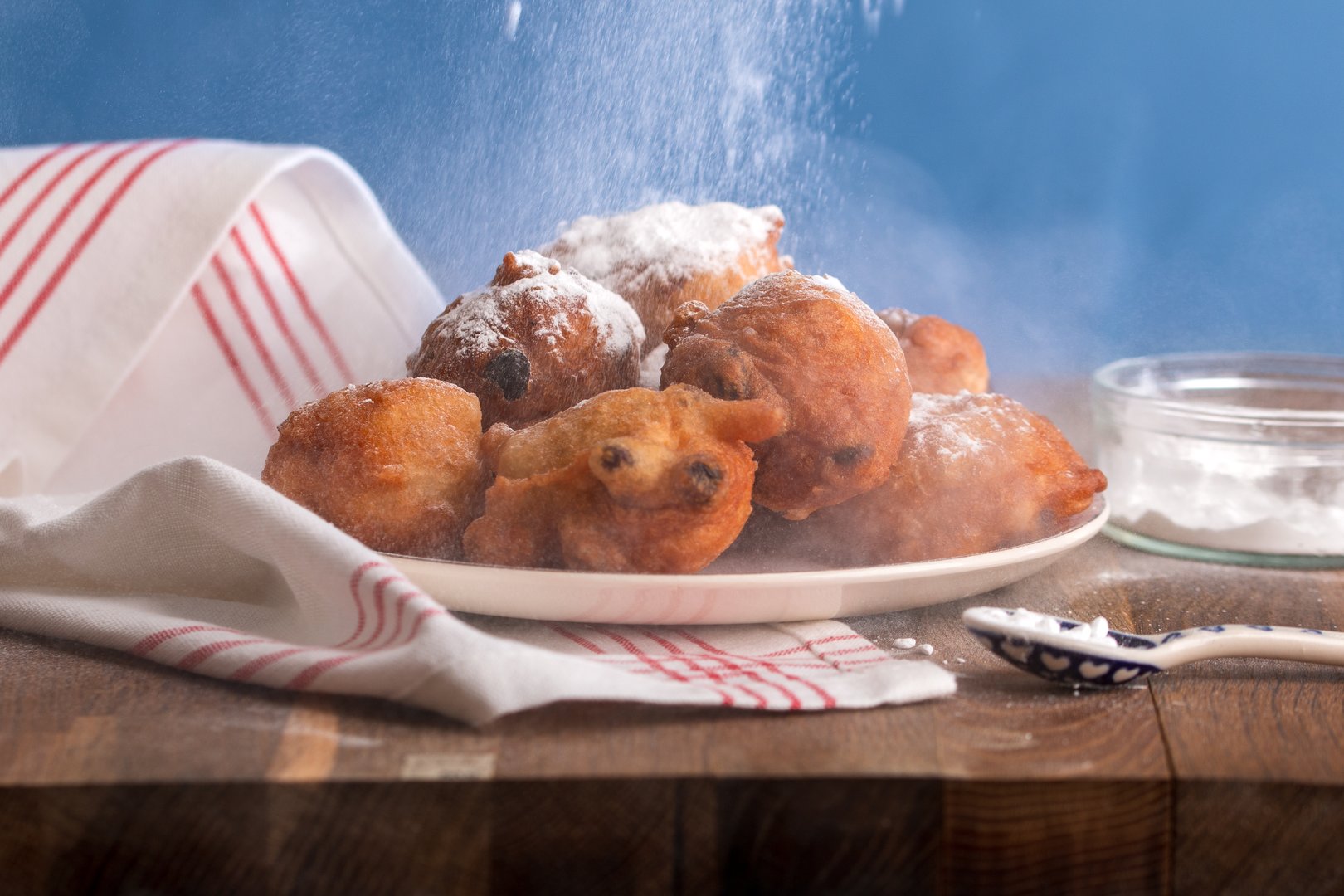 Delicious traditional freshly baked 'beignets' (oliebollen) for a perfect New Year's Eve.  An oliebol is a Dutch beignet, a variety of doughnut or fried dough that is traditionally eaten on New Year's Eve. Close up of a plate with oliebollen (beignets) sprinkled with powdered sugar, a typical Dutch traditional dish with New Year's Eve