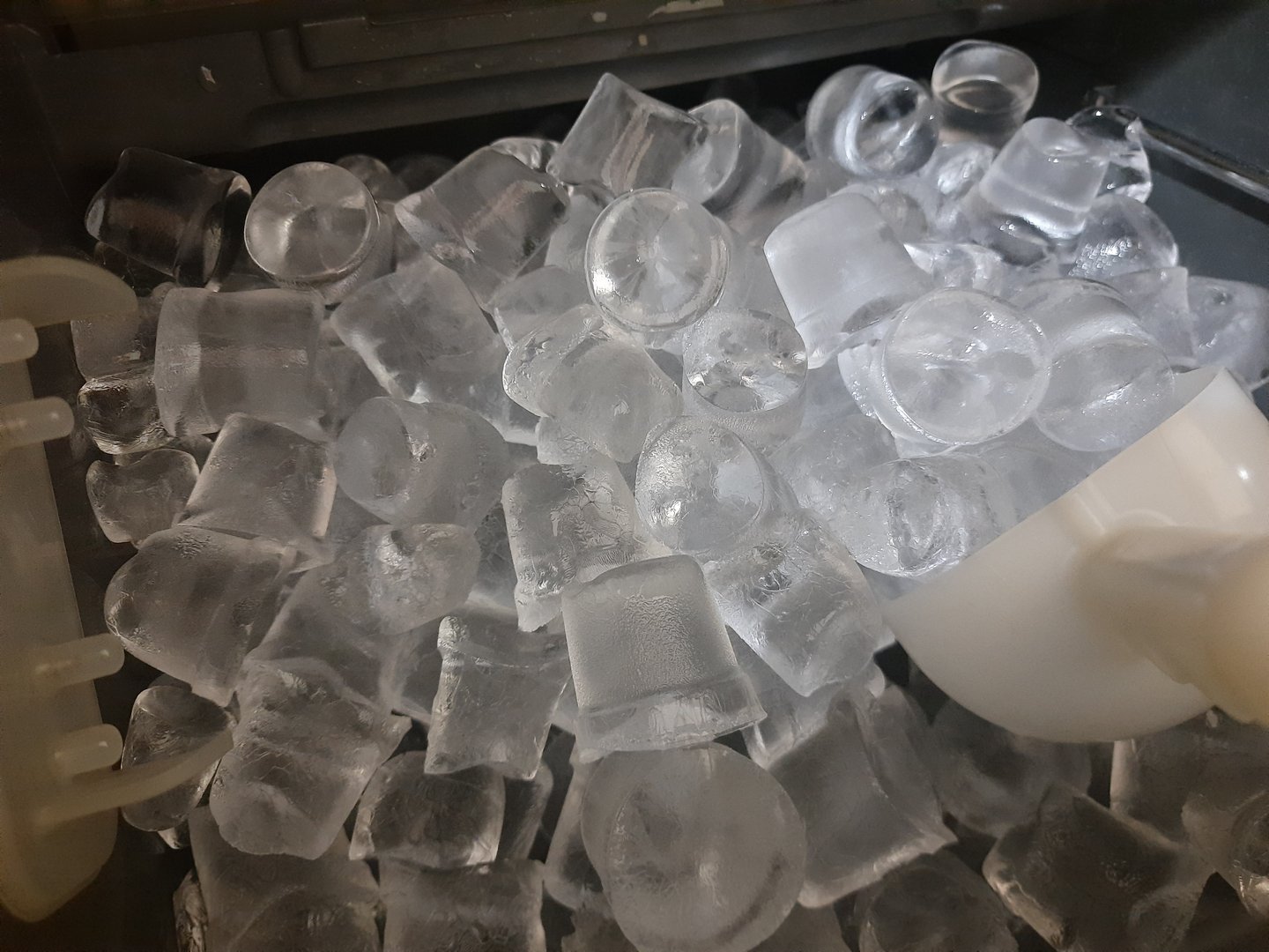 Pieces of ice and a white shovel inside an ice making machine. Close view