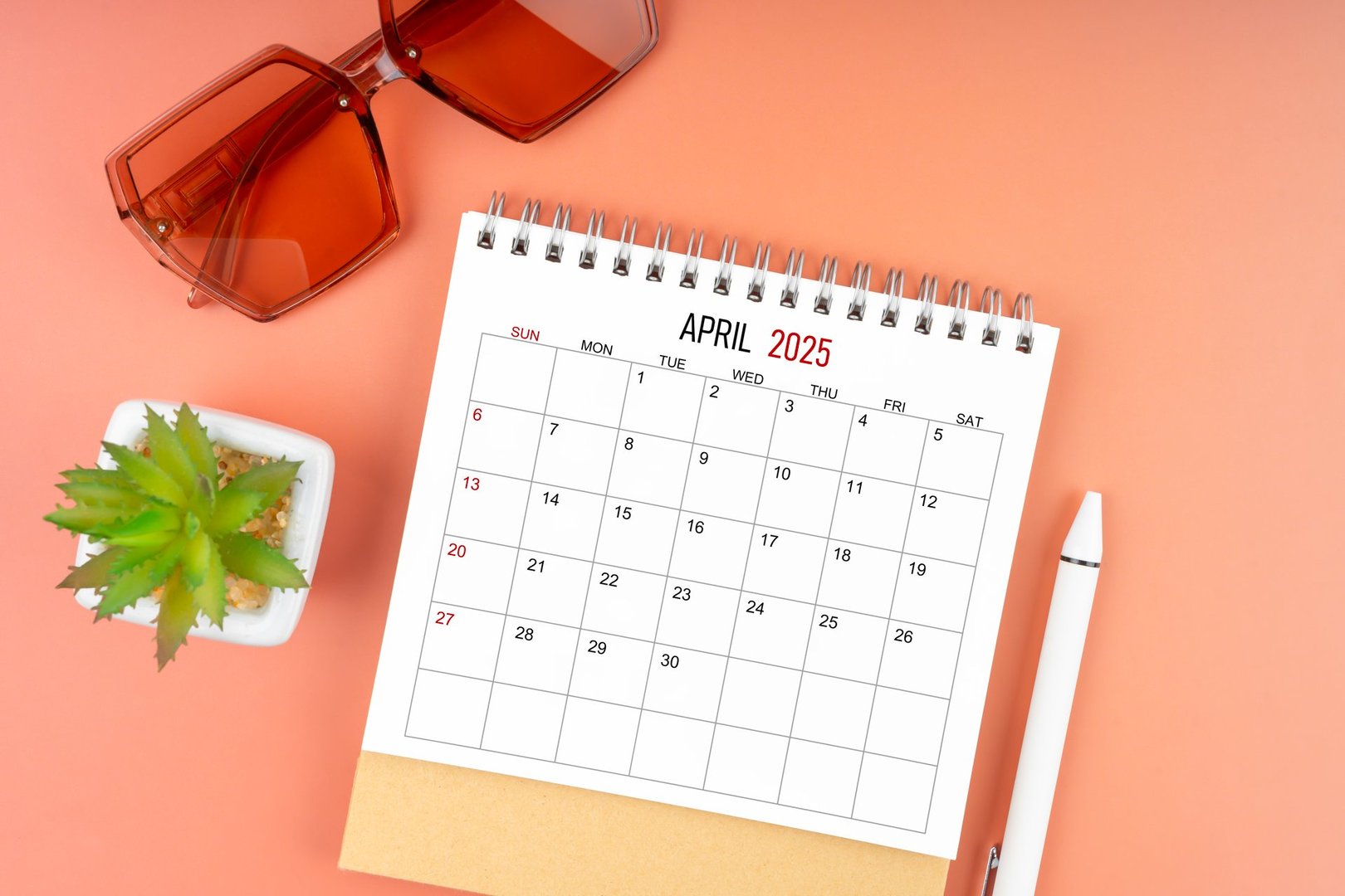 April 2025 desk calendar with brown sunglasses on beautiful background.