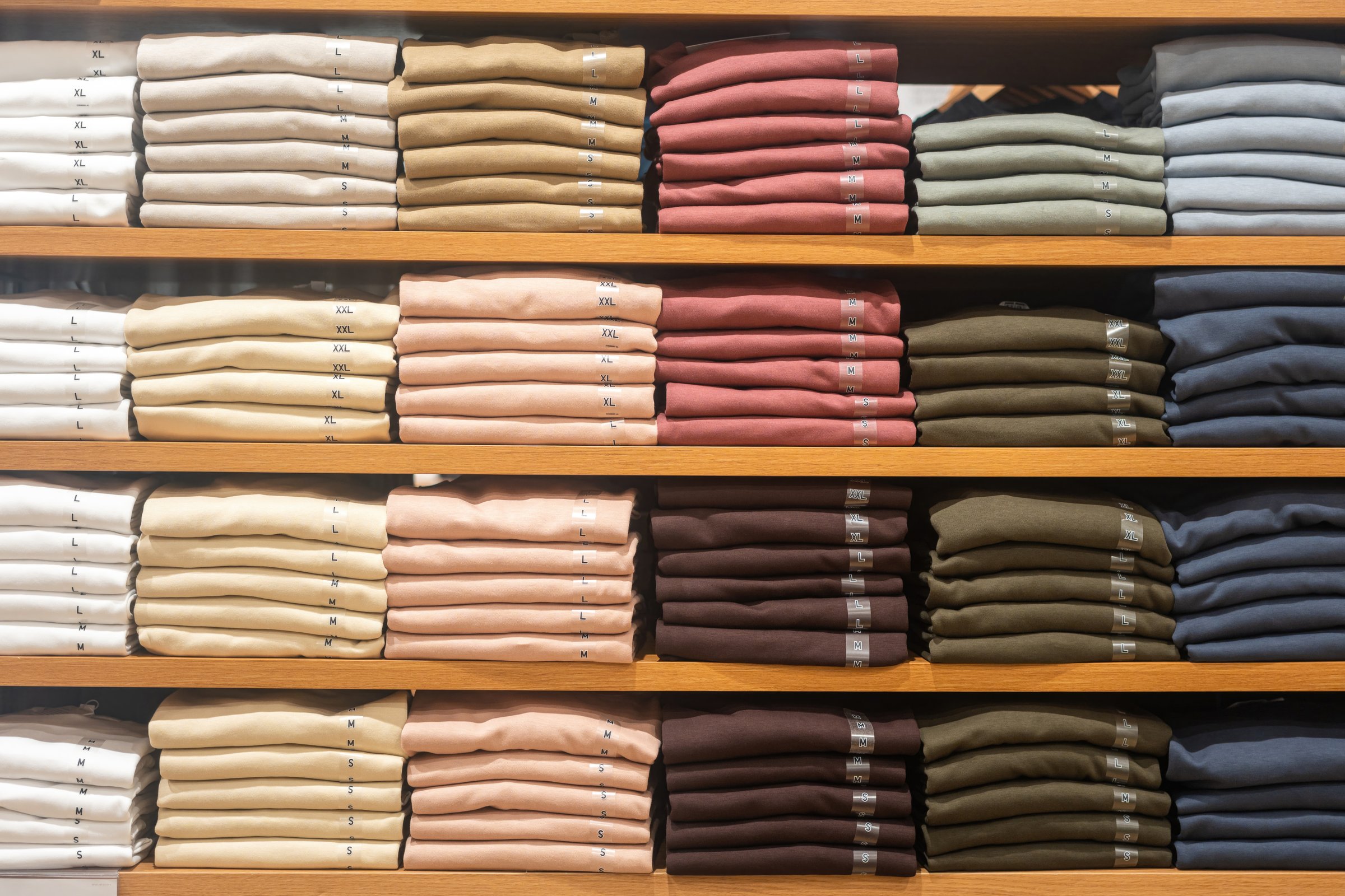 Cloths in various base color tone are folded on the shelf in clothing store