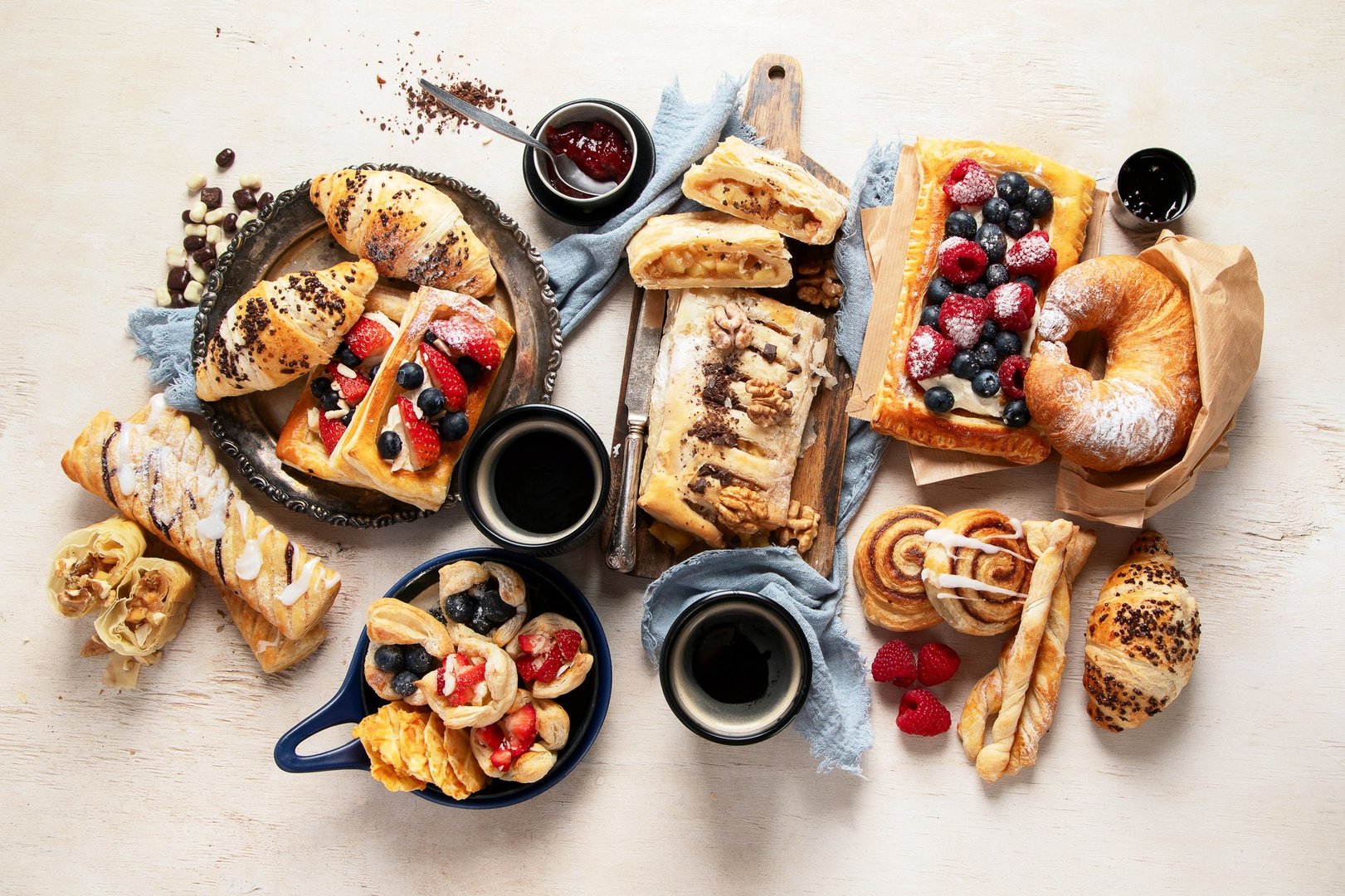 Table with various pastries and coffe cups on light backround. Top view.