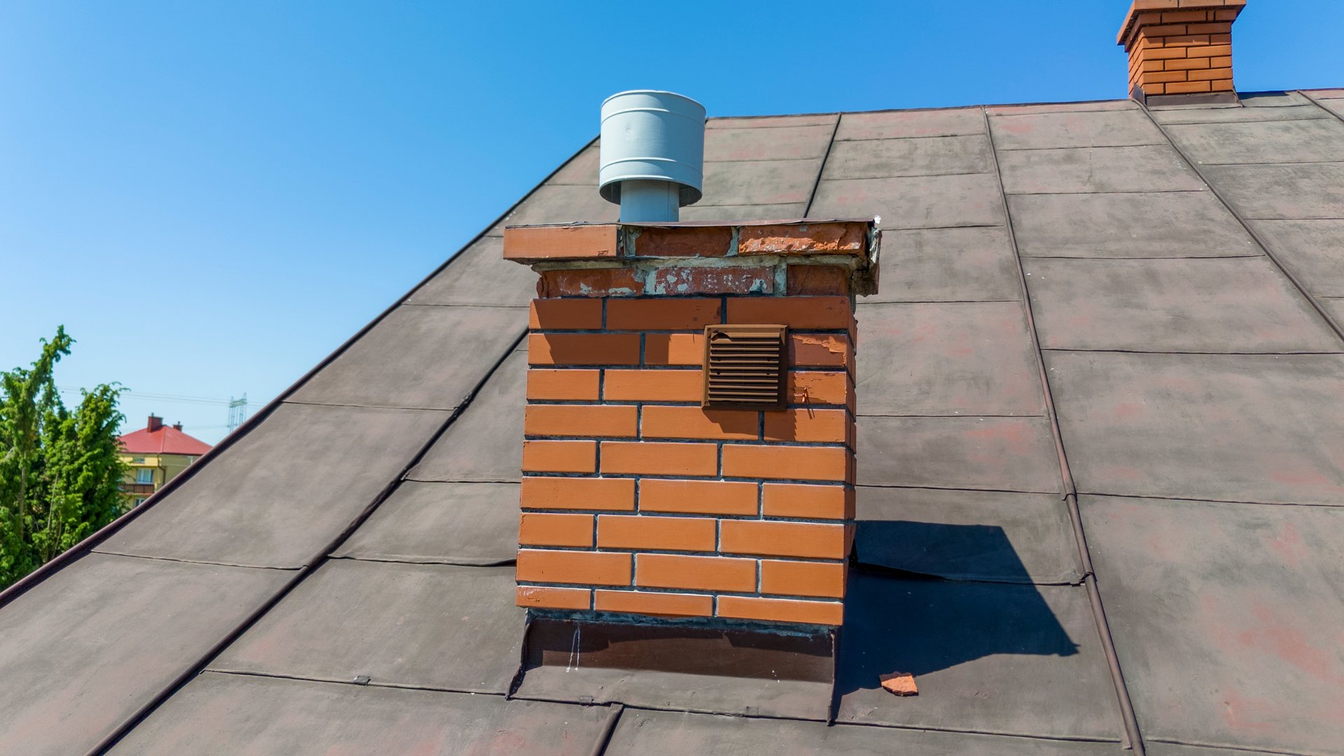 A close-up of a brick chimney on a roof against a clear blue sky. Perfect for home improvement, construction, and architecture themes.