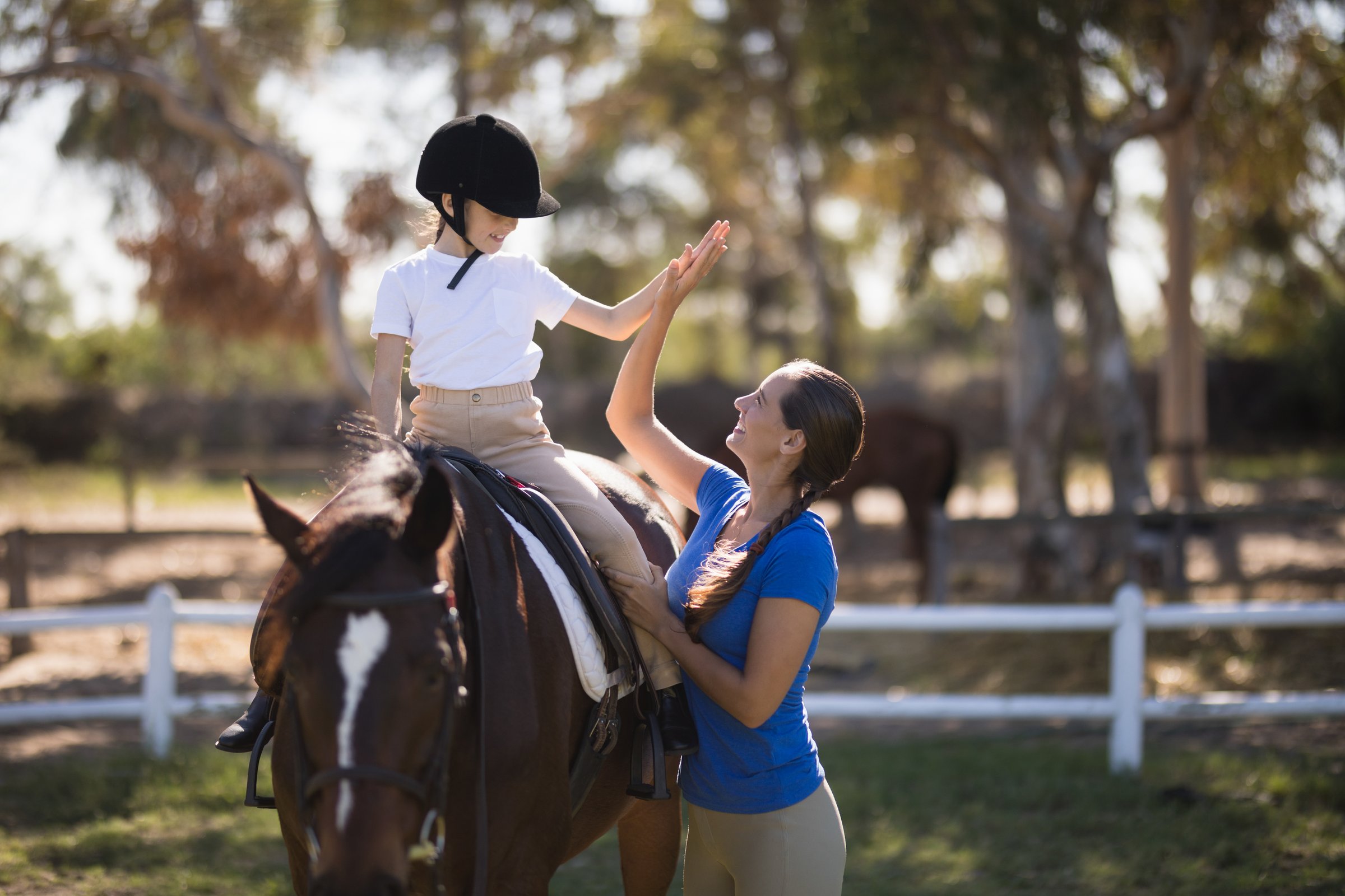 Meisje geeft high five aan instructrice tijdens paardrijles