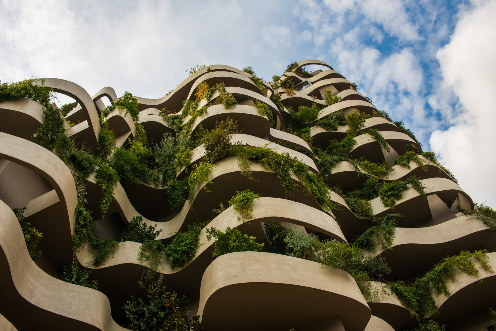 An organic-designed green building with curved balconies covered in lush plants, creating a vertical garden against the sky.