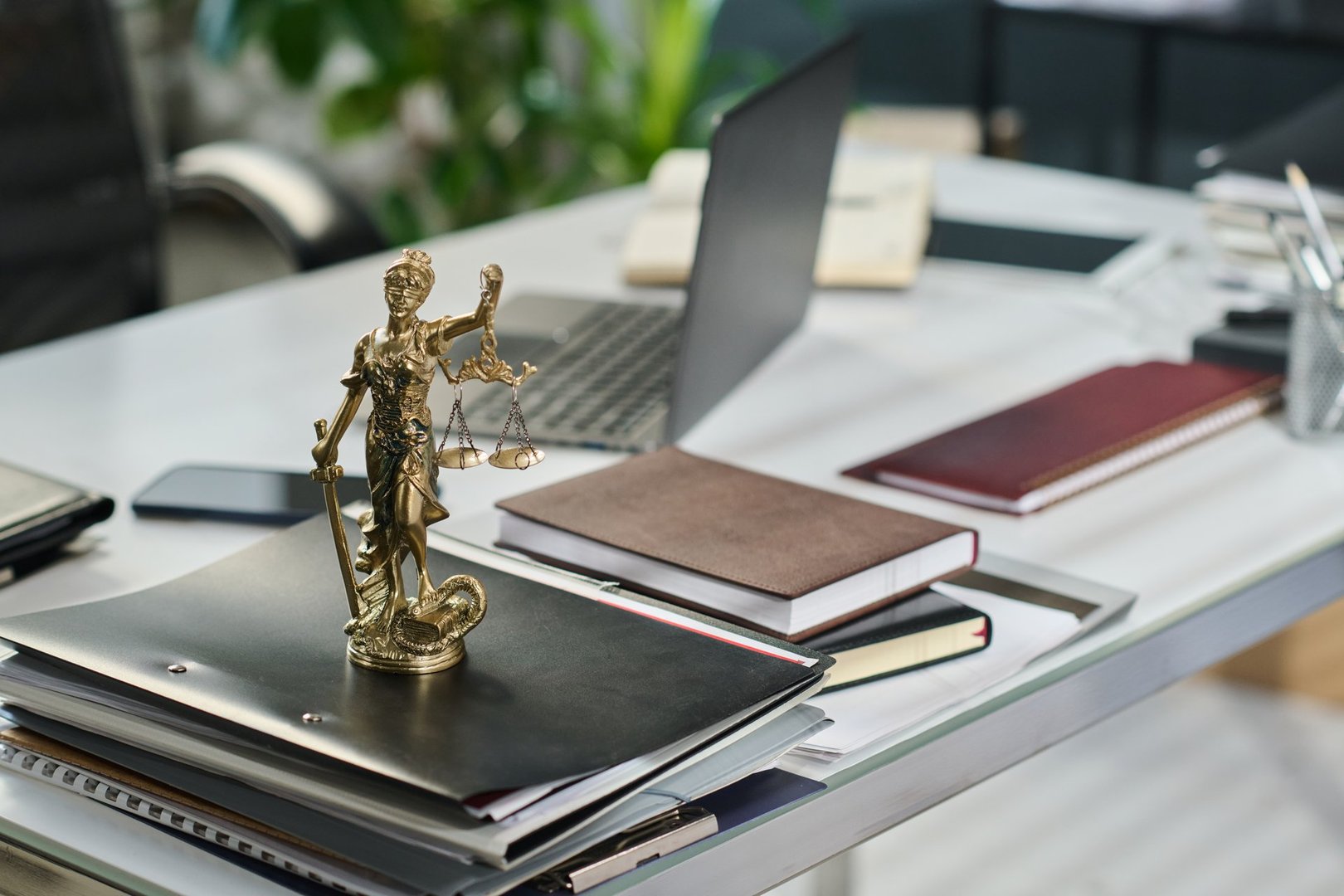 Small statuette of blindfolded goddess of Justice Themis with scale and sword in hands standing on stack of folders against other supplies