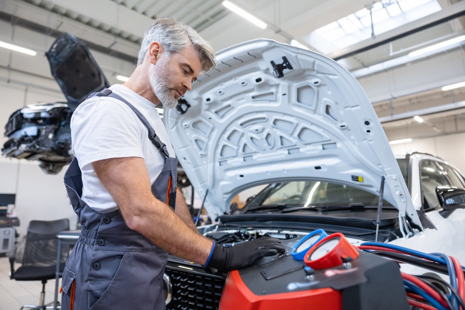 Bearded man mechanic in service shop using device measuring heat level in air conditioning system of car