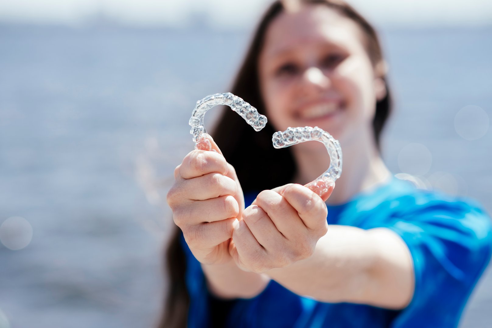 Dental care. Smiling woman holding heart-shaped aligners. Plastic retainers for teeth alignment.