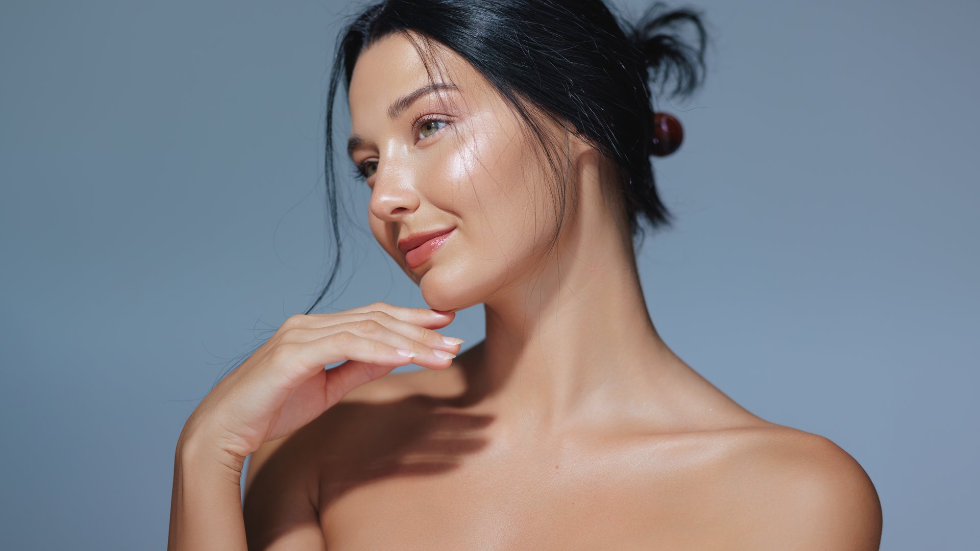 An elegant woman with natural makeup and glowing skin posing in a studio against a blue background. Perfect for beauty, skincare, and cosmetics promotions, this high-quality image features ample copy space for advertisements.