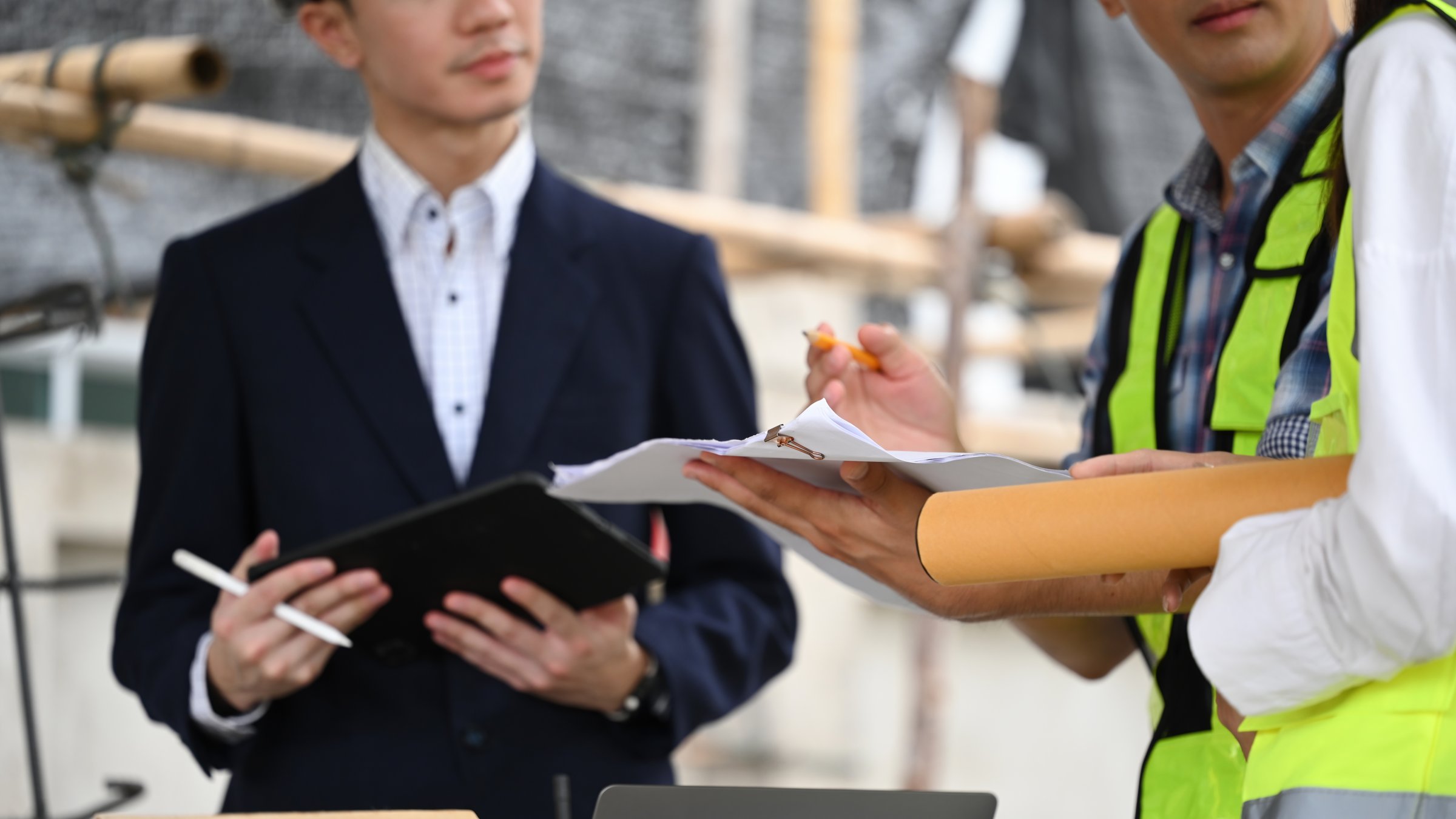 Close-up of a construction worker holding documents and discussing plans with the project manager, who is holding a tablet and pen.