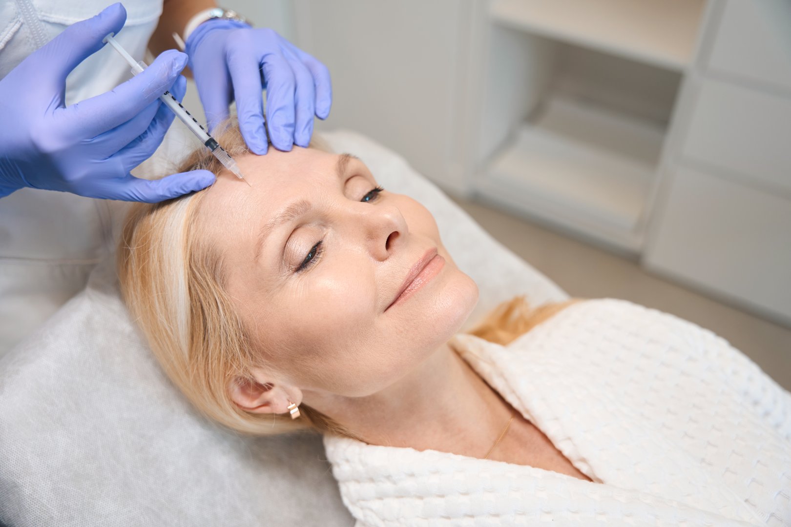 Close up of cosmetologist hands making rejuvenating injection for smoothing wrinkles on mature lady face in beauty salon