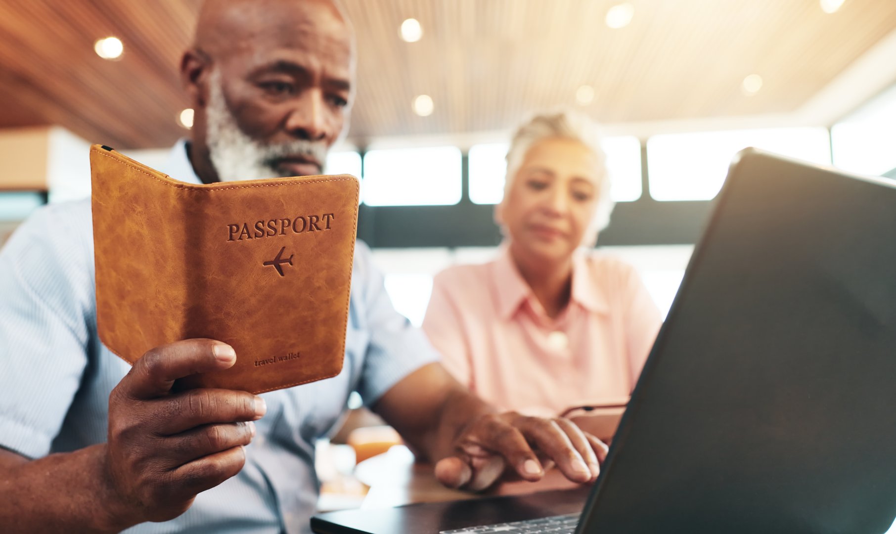 Senior couple, passport and laptop in home for immigration, identity or compliance for international travel. Interracial people, document and computer for flight booking with reading, search or date